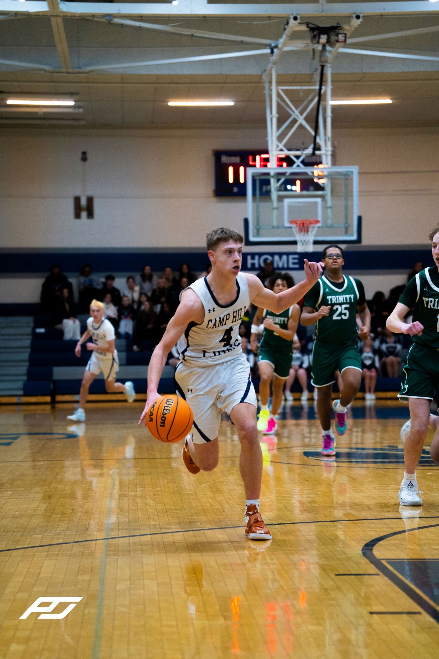 Camp Hill Lions guard drives to basket past Trinity defenders during high school basketball game.
