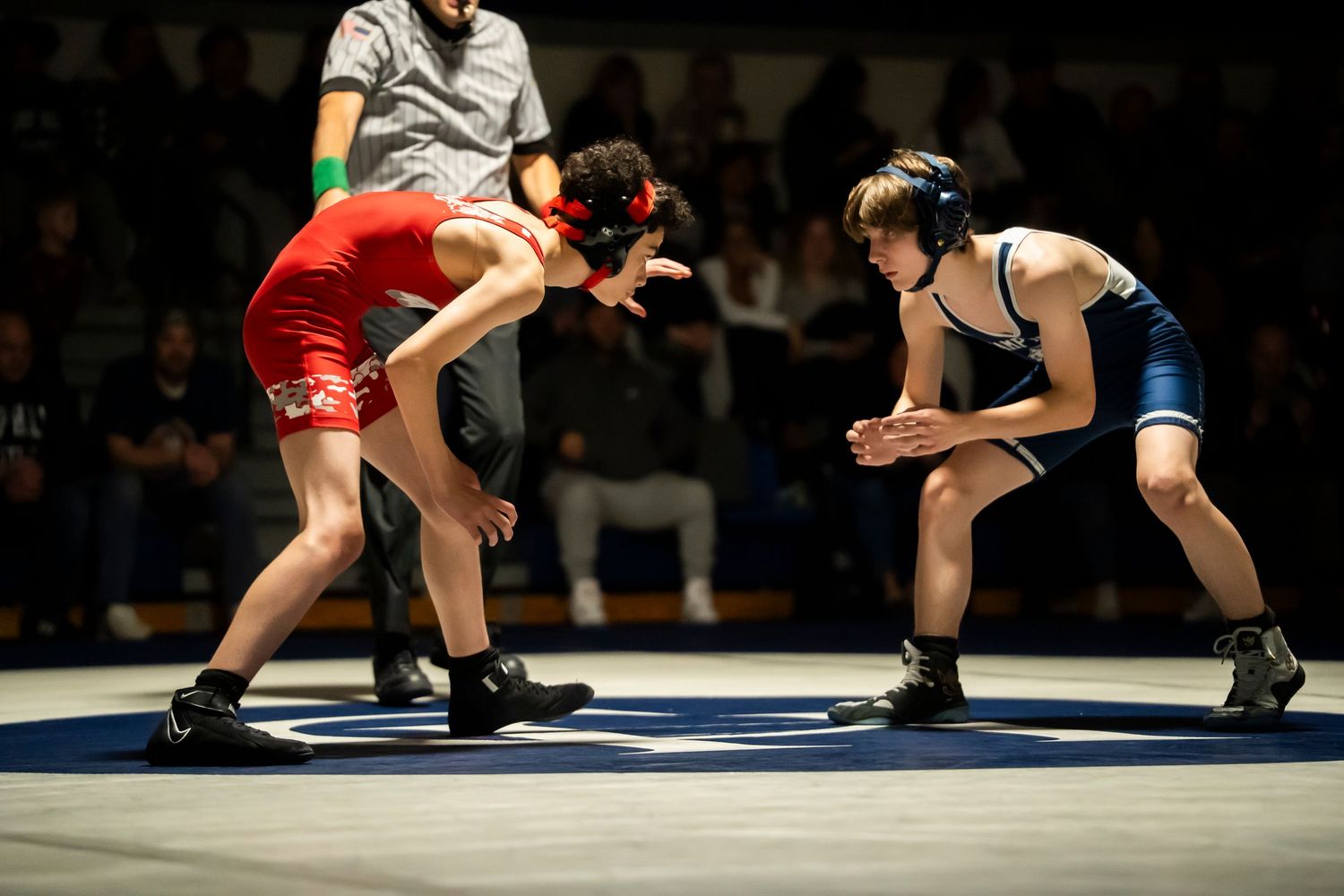 Two youth wrestlers in red and blue singlets face off in a competitive wrestling match.
