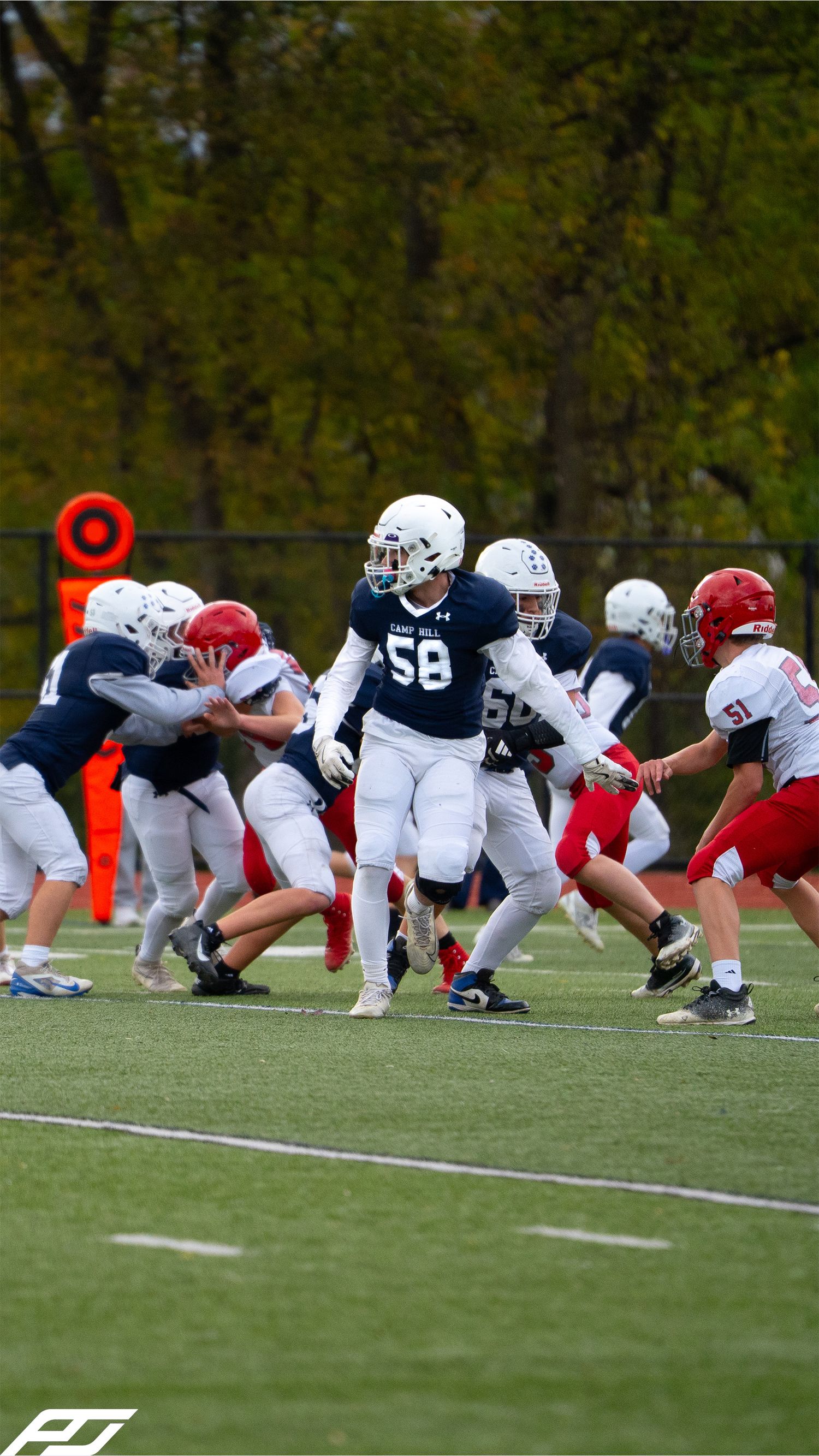 Youth football lineman number 58 in navy uniform engages in blocking during a game against red-uniformed opponents.