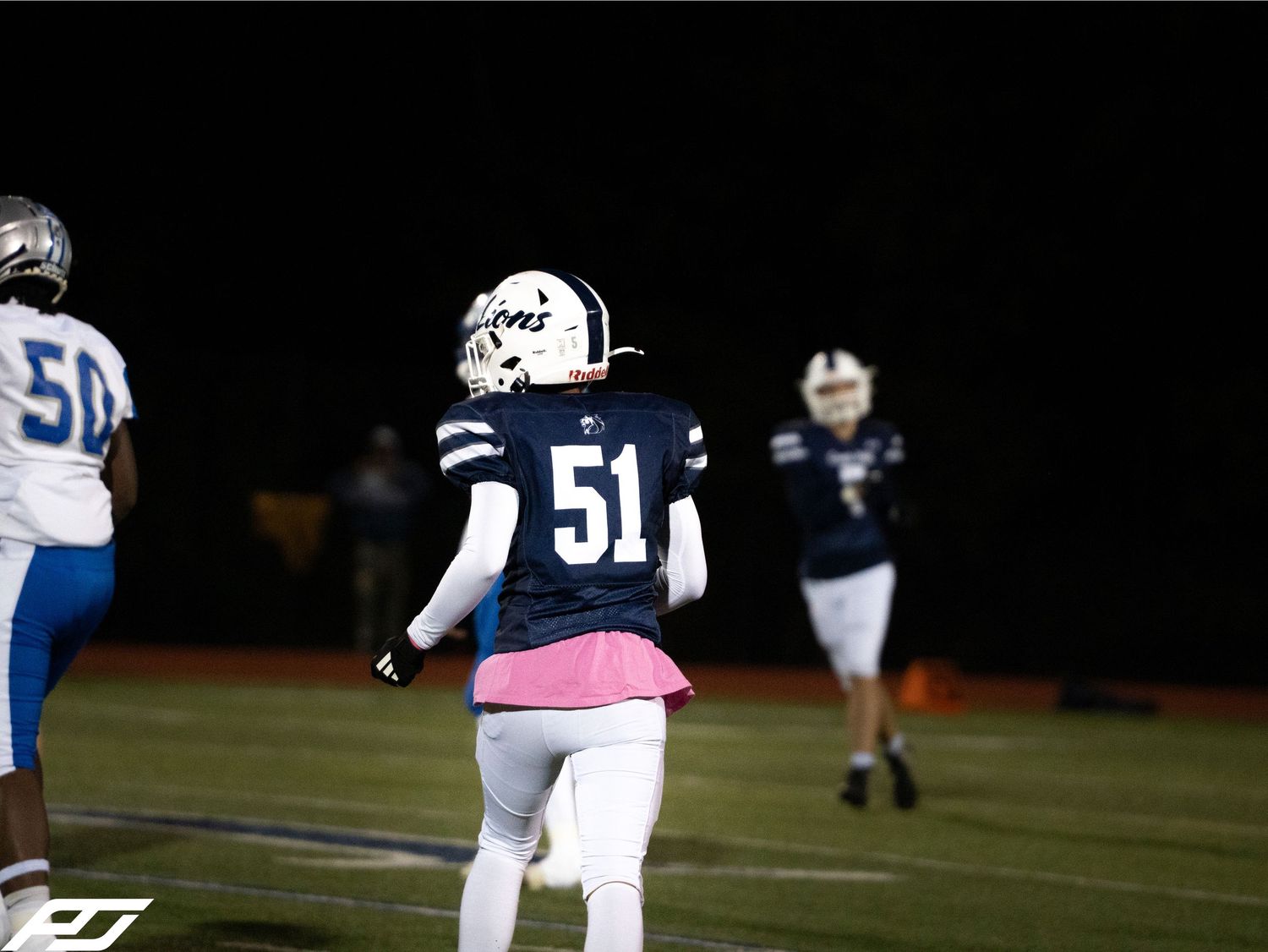 High school football player wearing navy Lions jersey number 51 walks on field during night game.