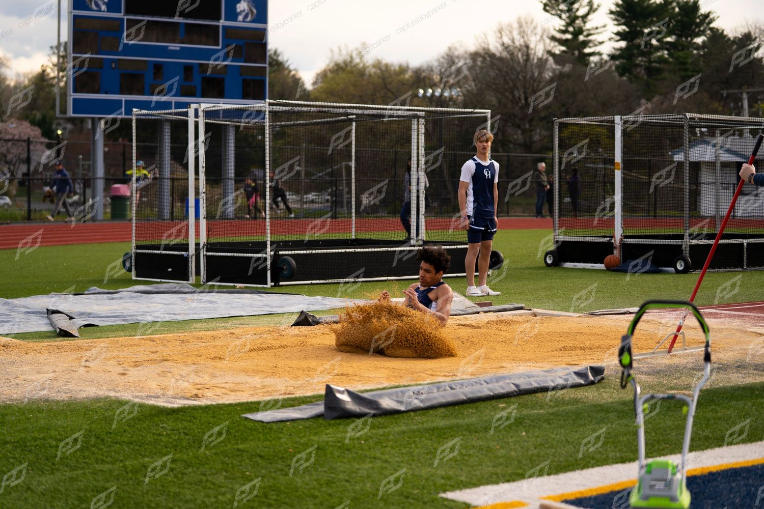 Track and field athlete lands in sand pit during long jump competition at high school outdoor meet.