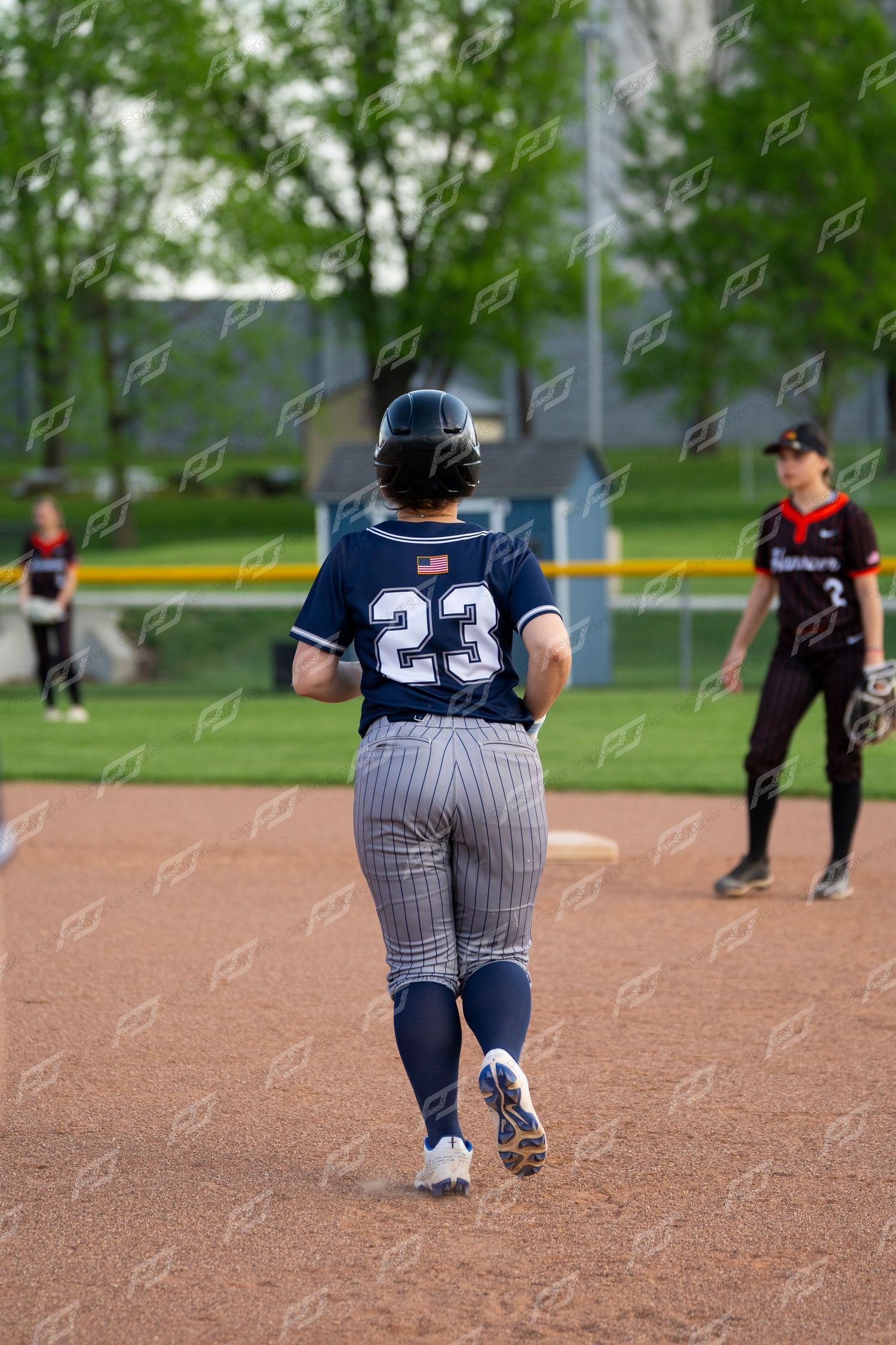 Softball player number 23 in navy pinstripe uniform runs bases during an outdoor game.