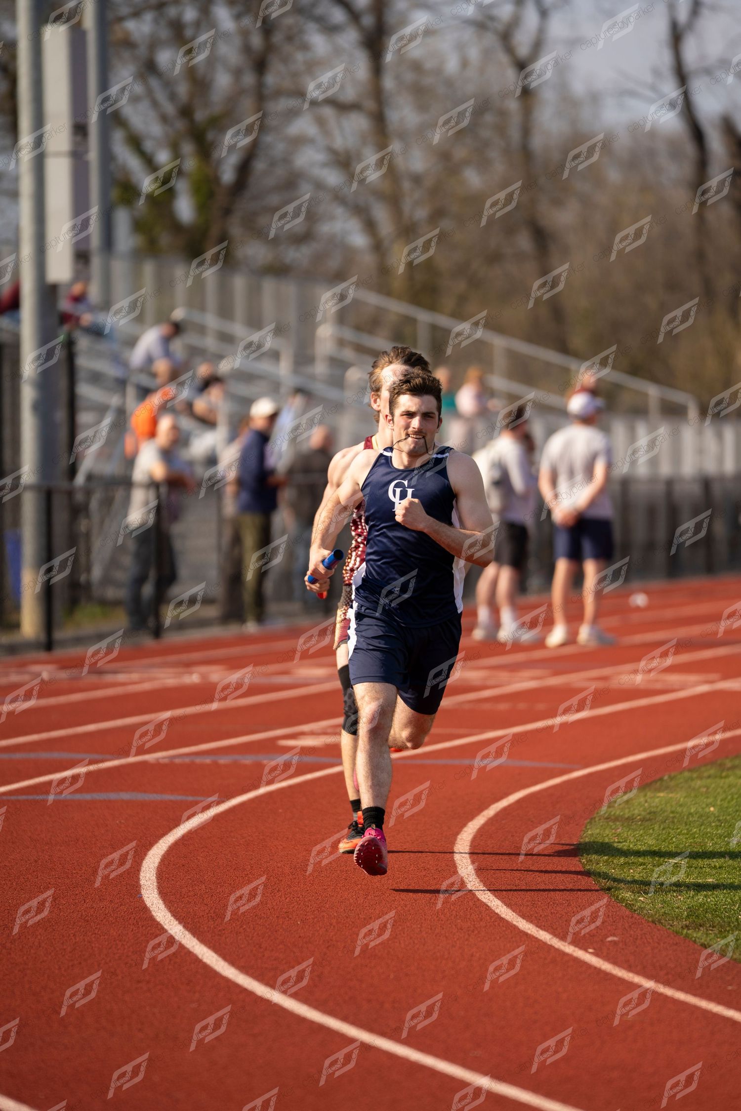 Male distance runner in navy singlet competing on red outdoor track during a meet.