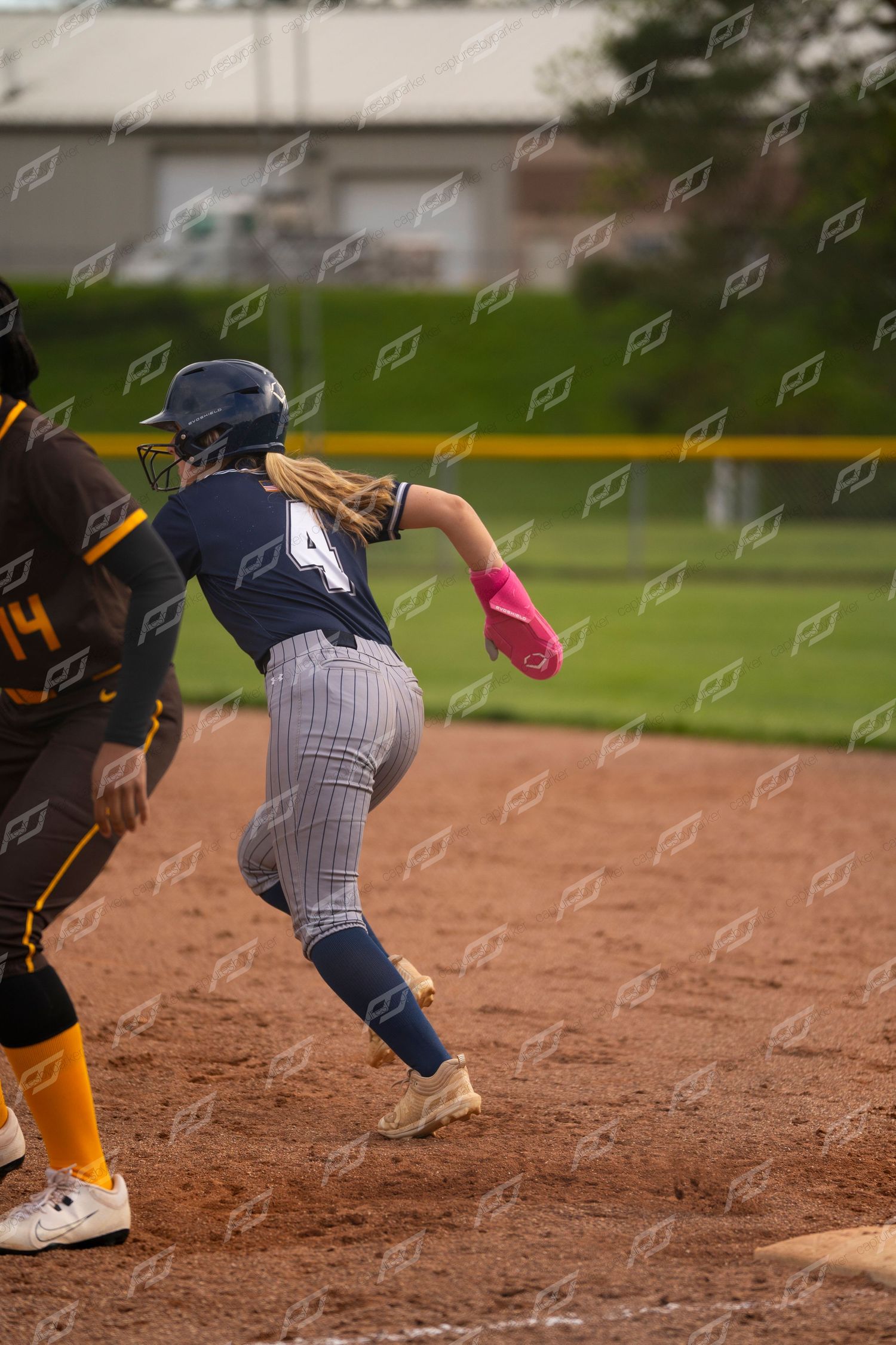 Softball player number 4 runs past first base during a competitive game against opponents.