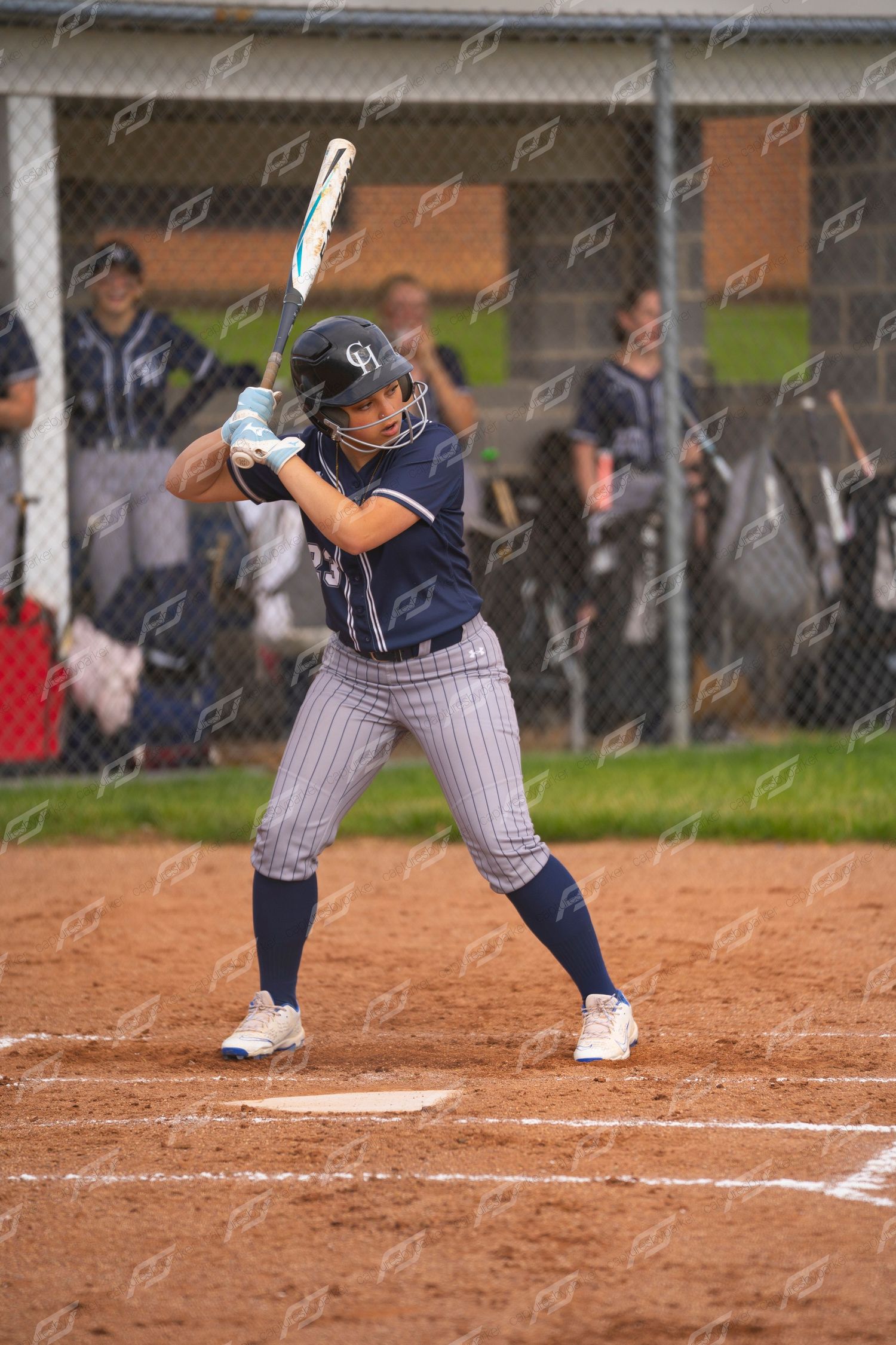 Female softball player in navy pinstripe uniform stands ready at bat during a game.