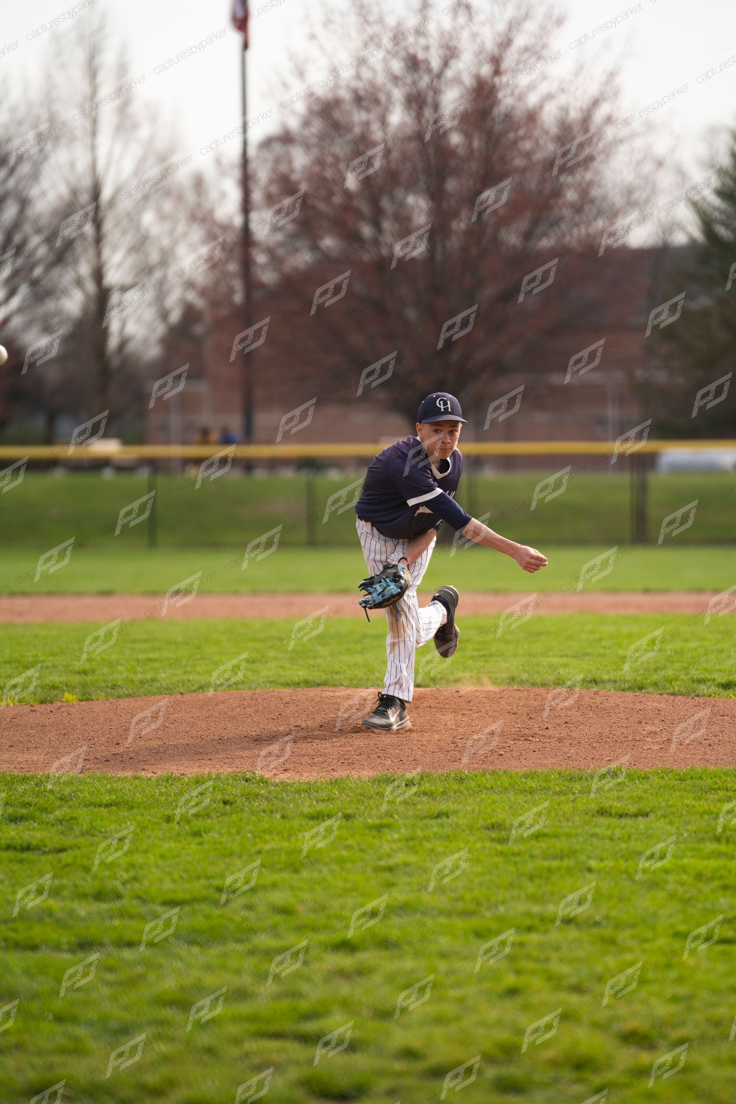Young baseball pitcher in navy pinstripe uniform completing a full follow-through after delivering a pitch.