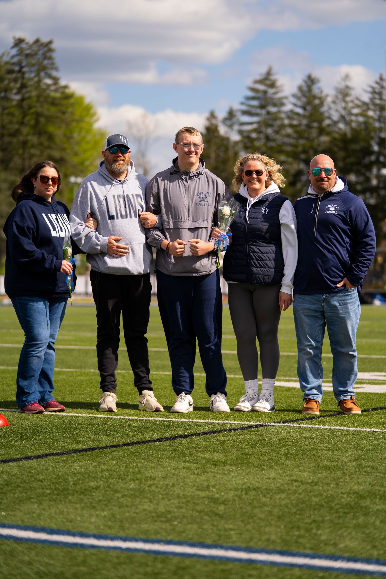 Five people pose together on a football field during a school sports senior day celebration.