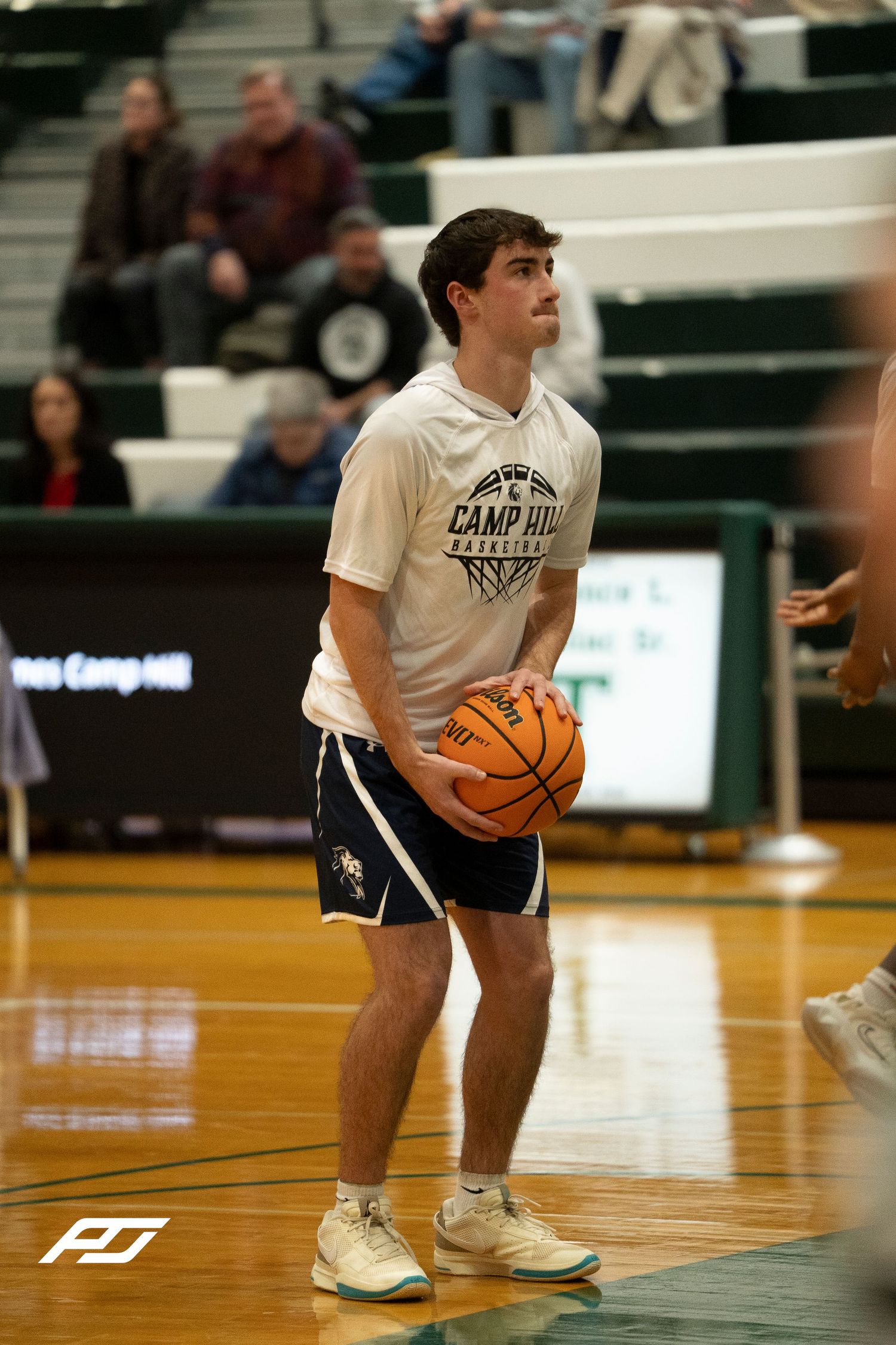 Camp Hill Basketball player in white warmup shirt prepares to shoot during pre-game warmups in green gym.