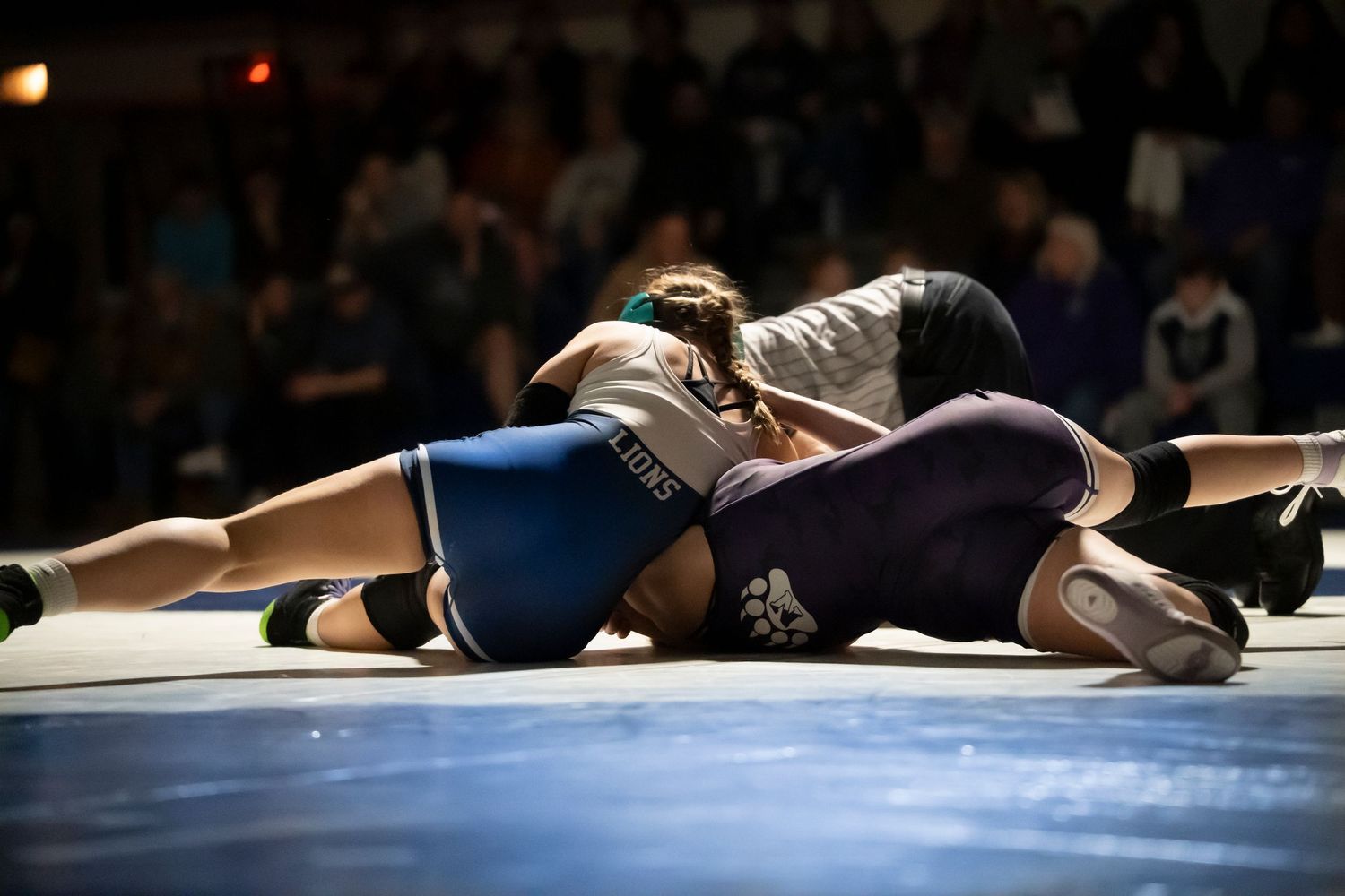 Wrestler in blue singlet attempts to pin opponent to the mat during a wrestling competition.