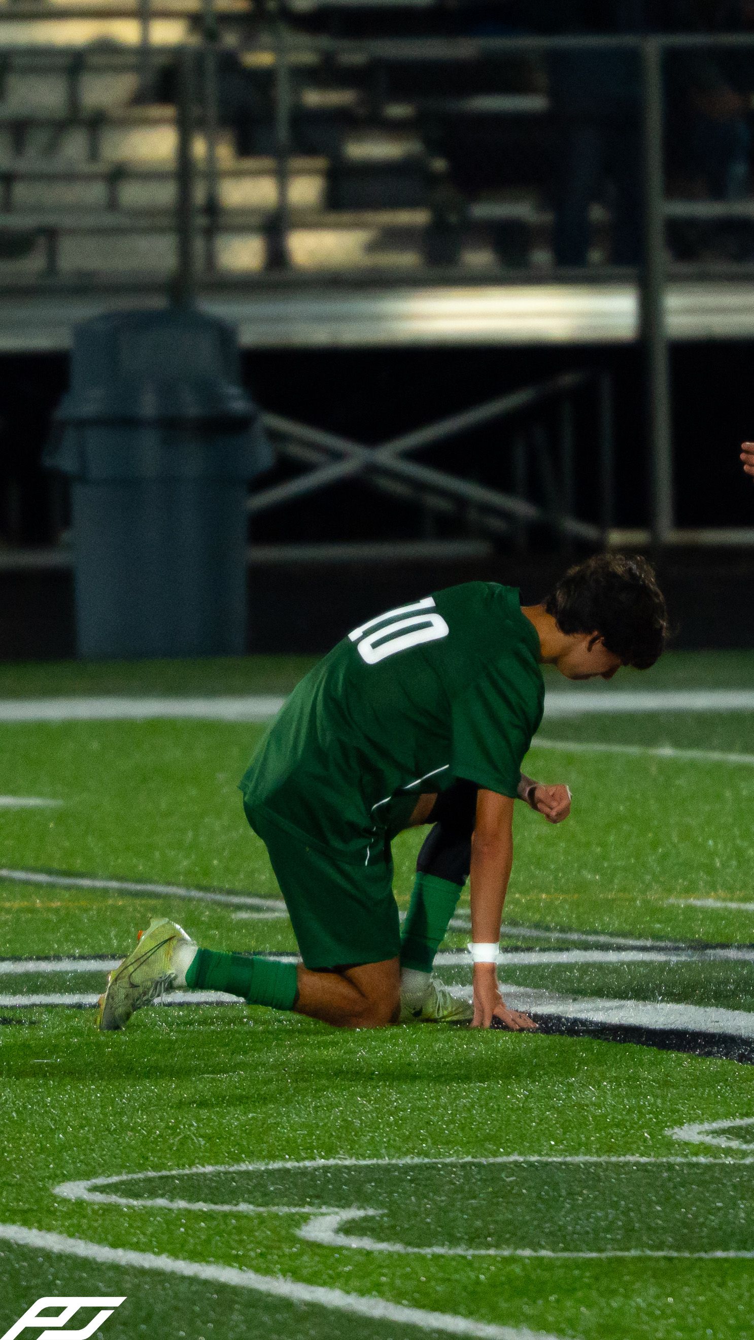 Trinity soccer player #10 in green uniform kneeling on turf field during a night game.