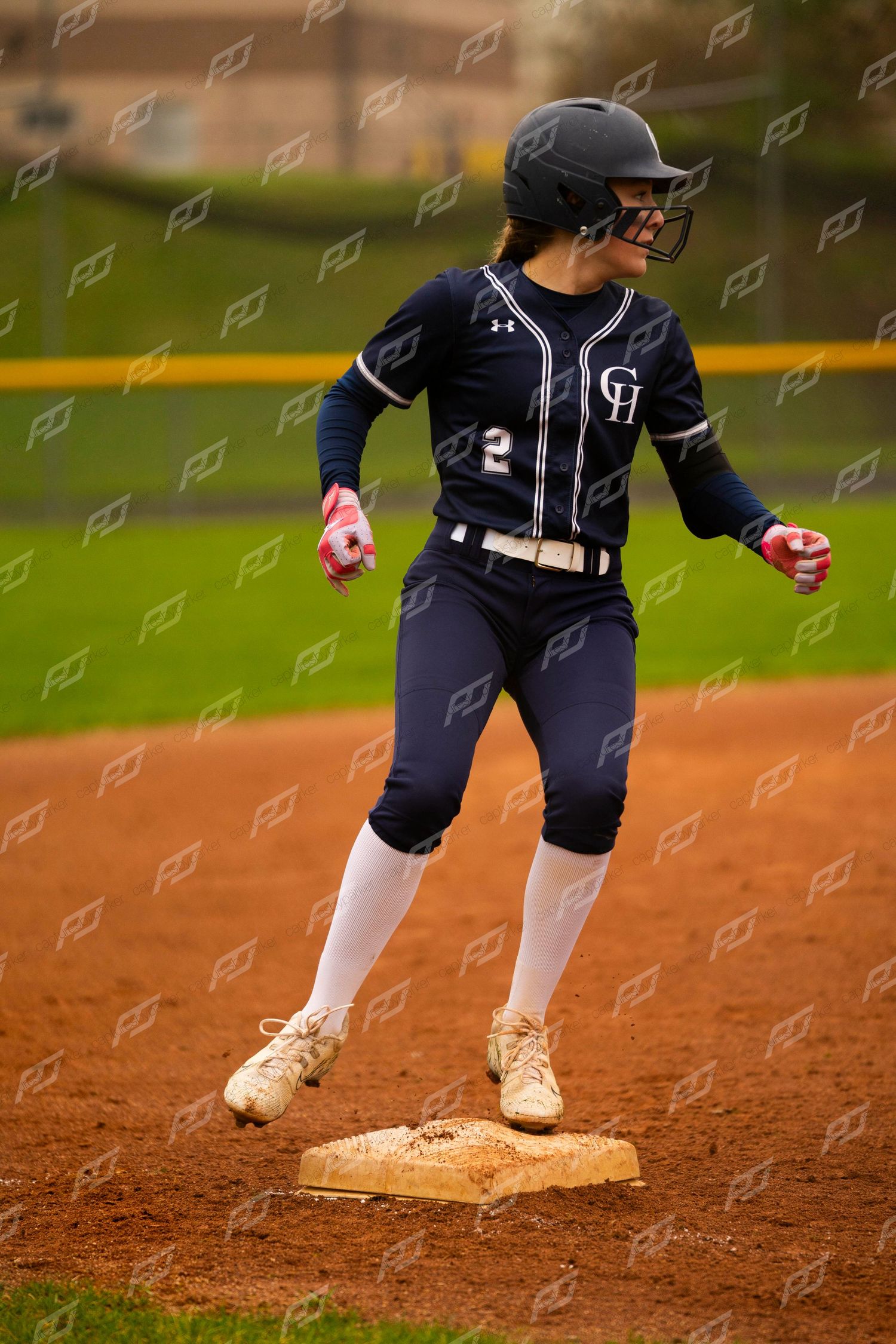 Female softball player in navy uniform rounds a base during a game.