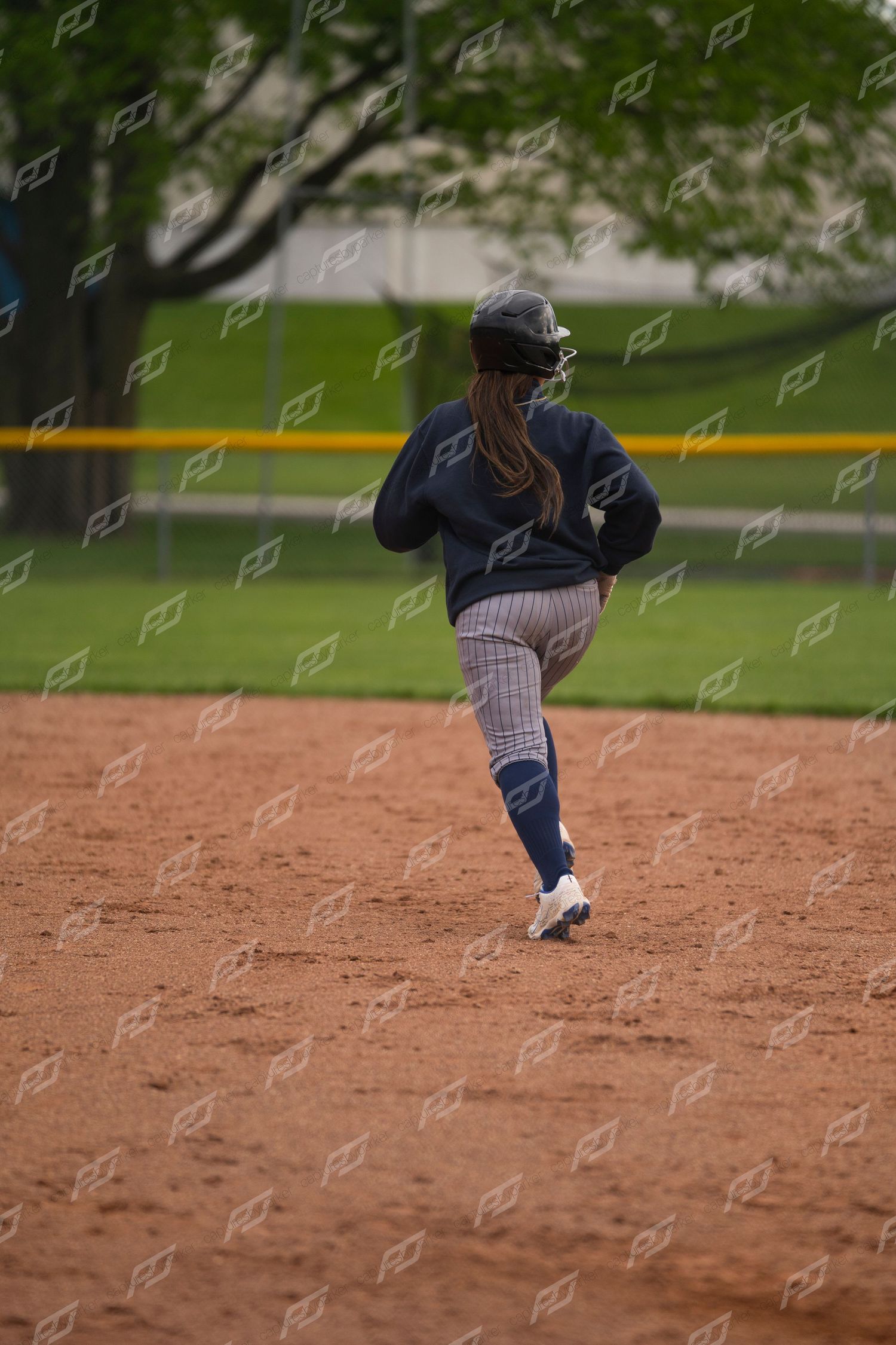 Female softball player running the bases on a dirt infield during an outdoor game.