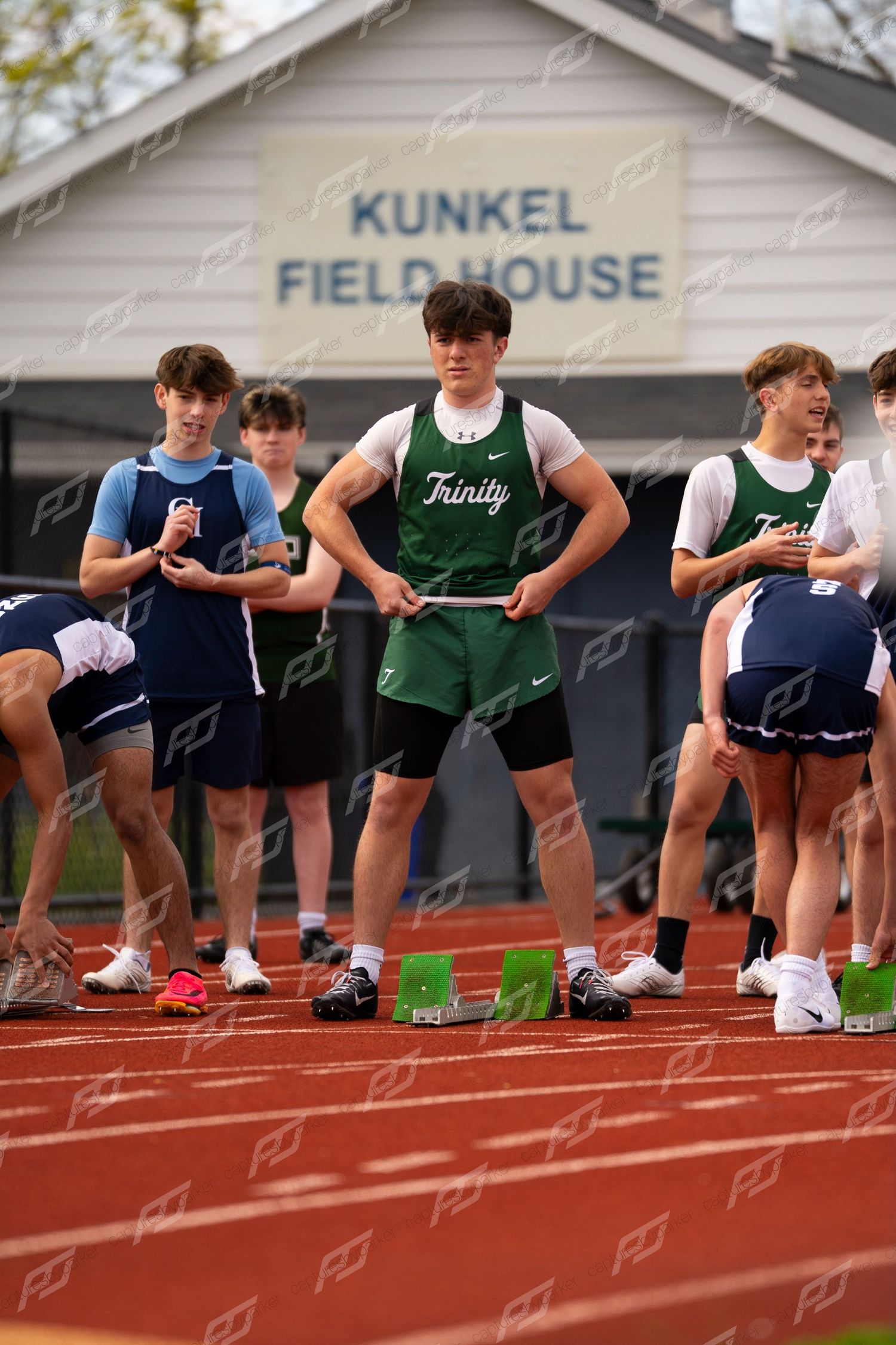 Male Trinity track athlete in green uniform stands at starting blocks at Kunkel Field House meet.