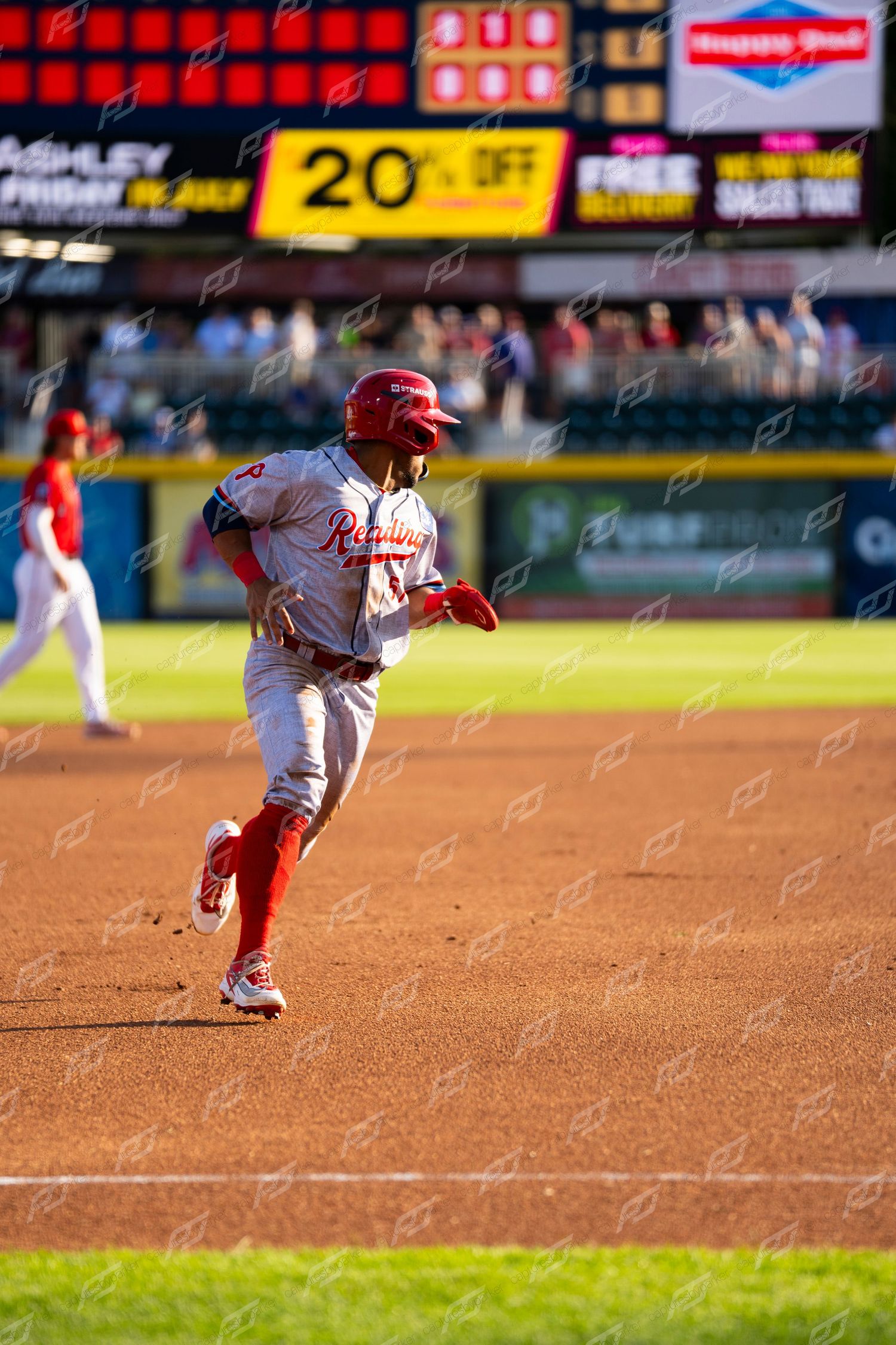 Baseball player in red Phillies uniform rounding the bases during an evening game at the stadium.