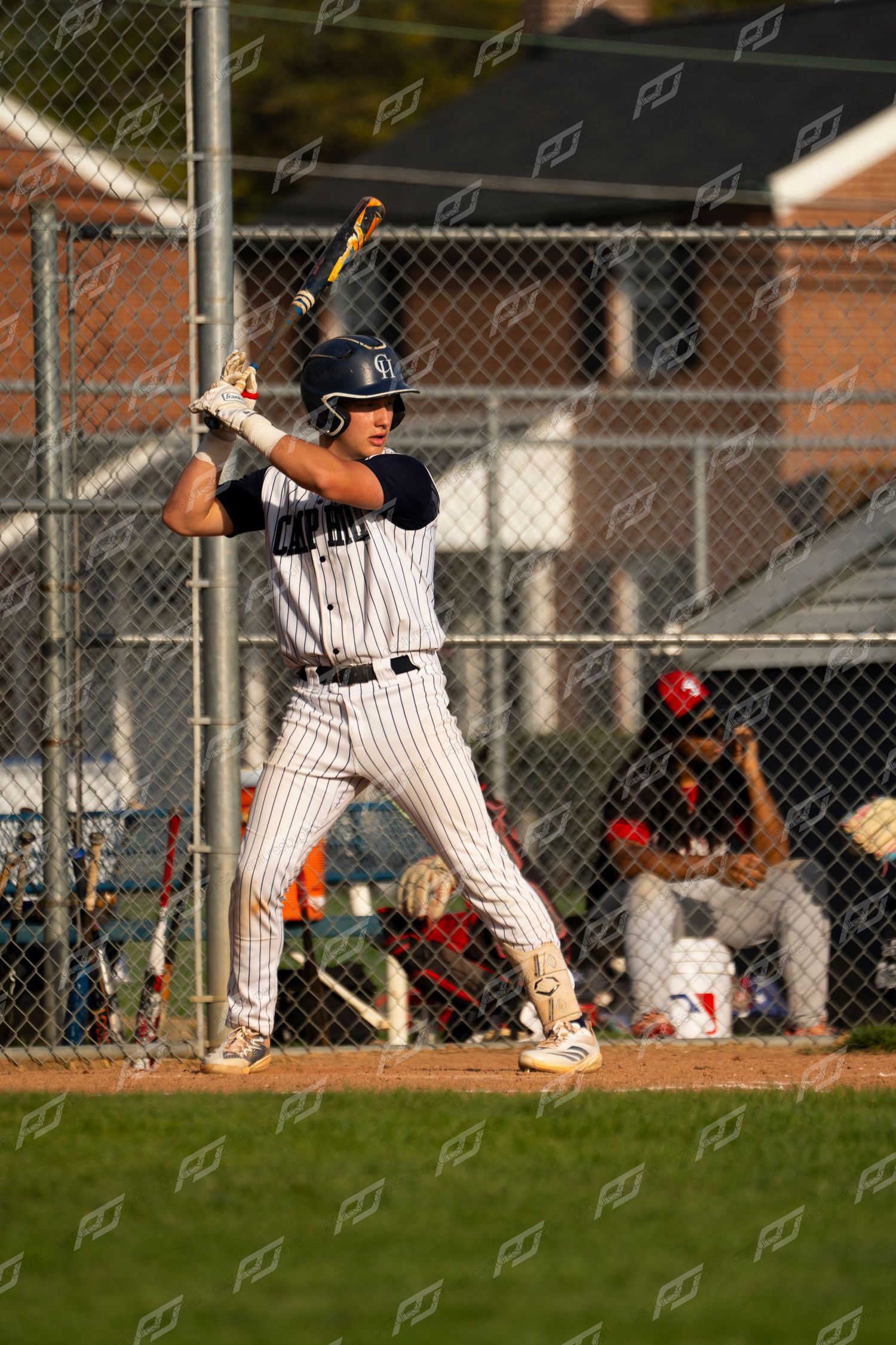 Youth baseball batter in pinstripe uniform stands ready at the plate in an athletic batting stance.