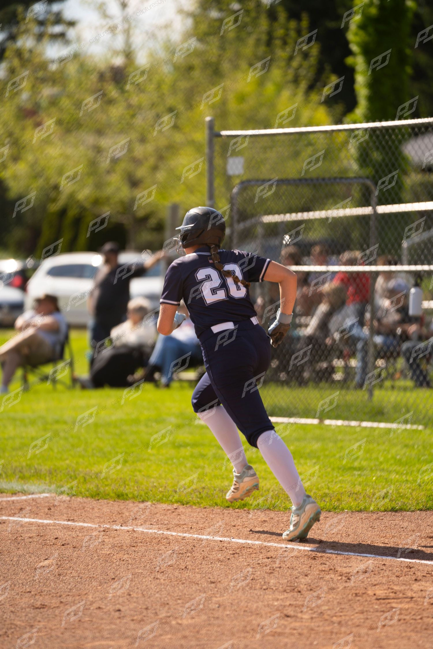 Softball player number 20 in navy uniform sprints along the baseline during a game.