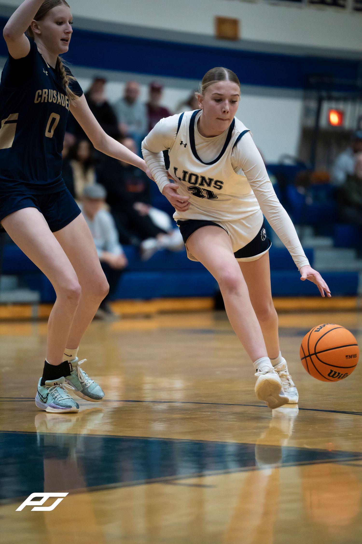 Female Lions basketball player dribbles past a Crusaders defender during a high school girls basketball game.