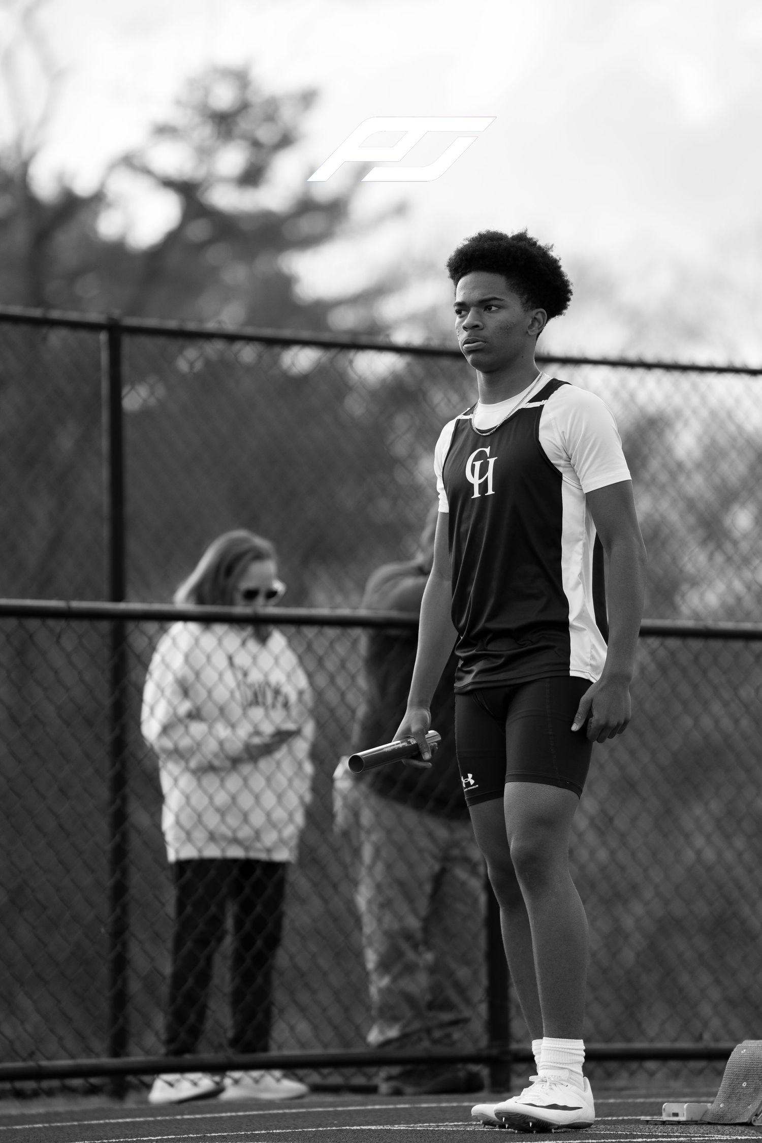 Male high school track athlete holds relay baton while standing on outdoor running track.