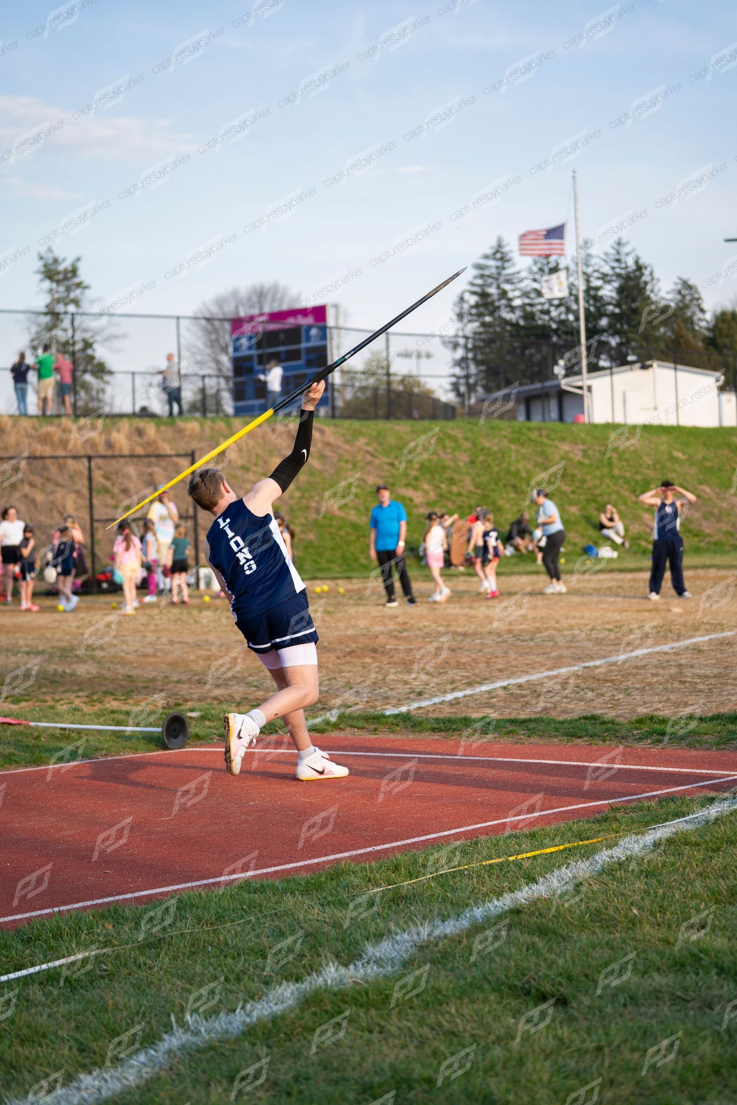 A high school javelin thrower launches the javelin at an outdoor track and field competition.