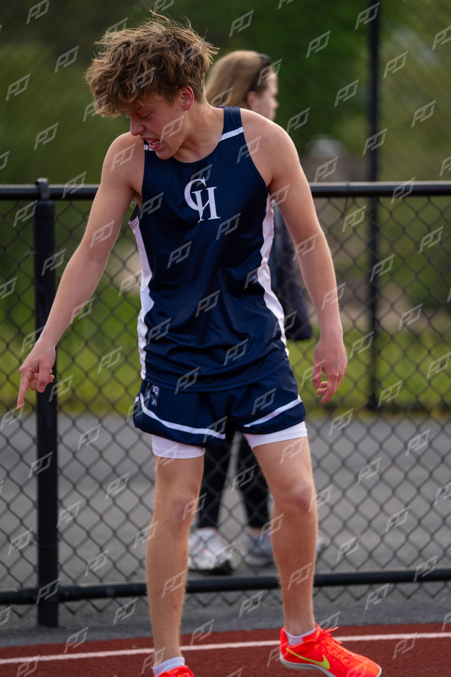 Male track athlete in navy uniform bends forward catching breath after a race.