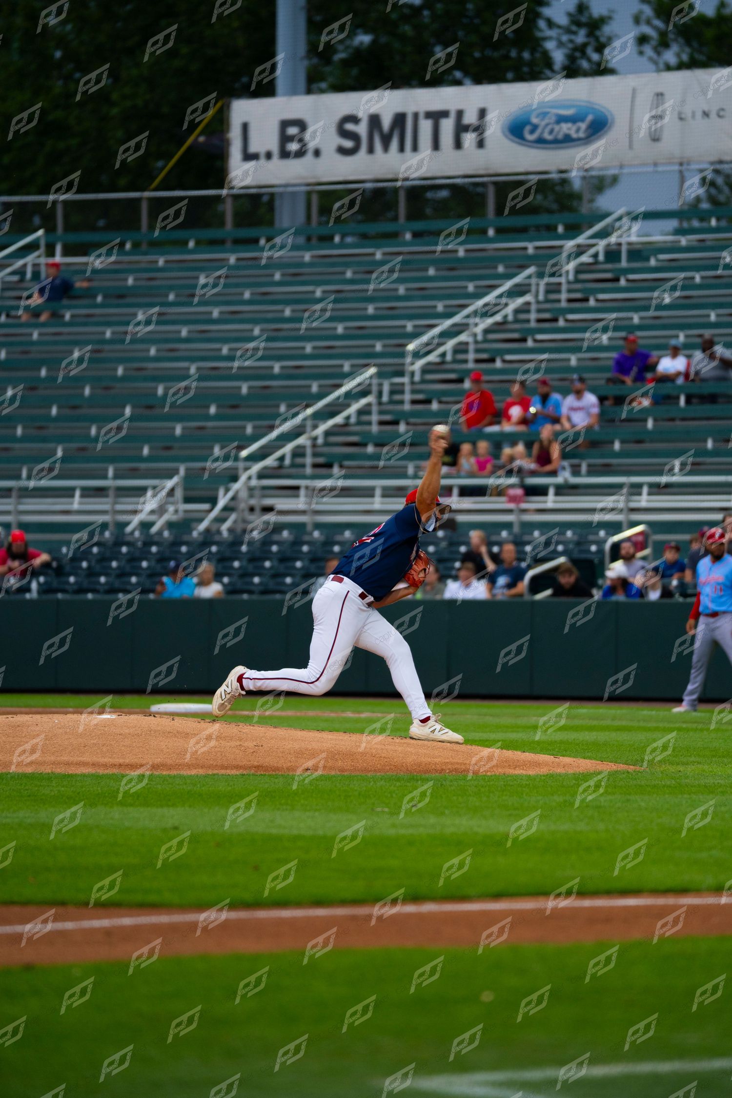 Minor league baseball pitcher in navy uniform throwing a pitch from the mound during a game.