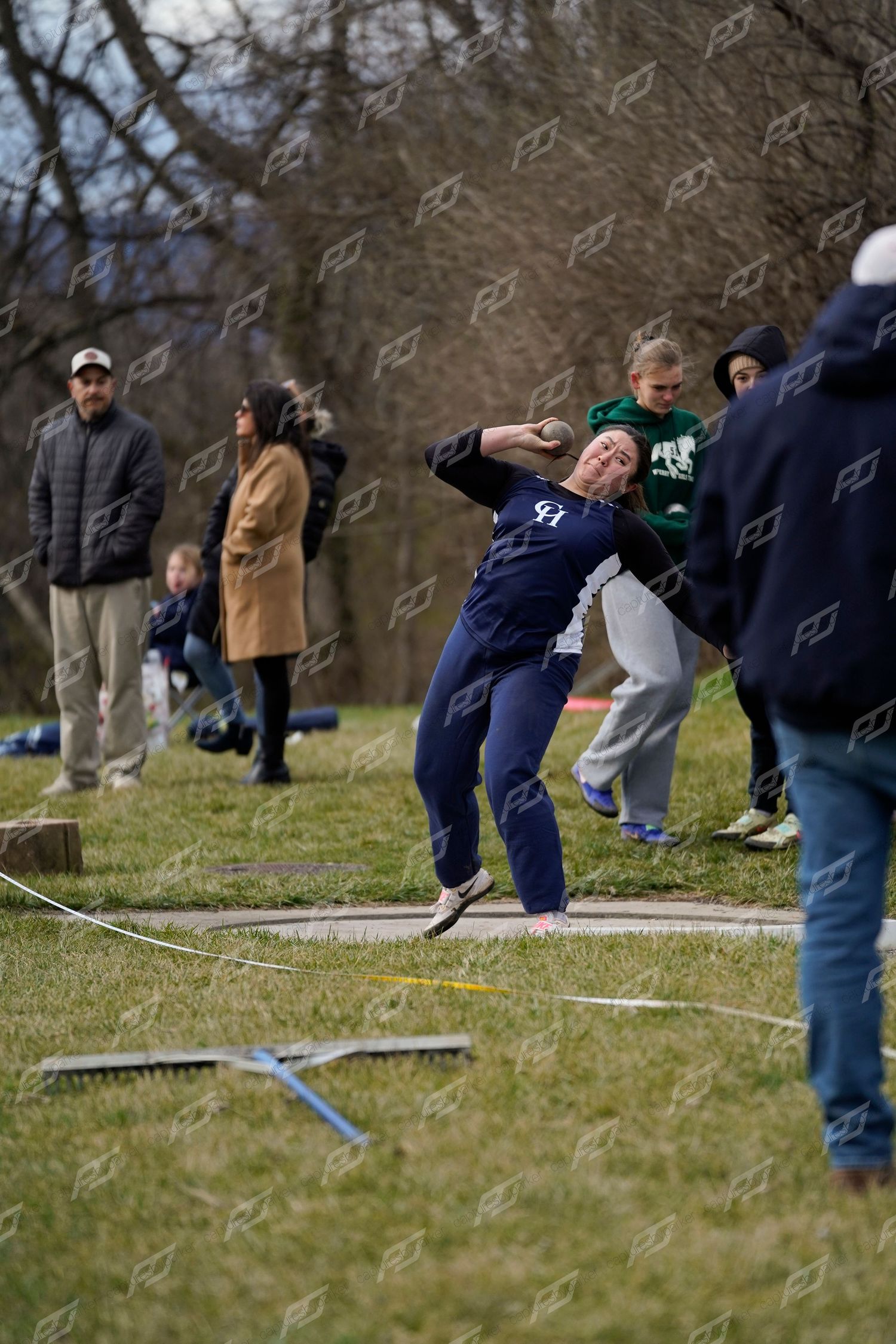 Female athlete in navy uniform throwing shot put at an outdoor track and field competition.
