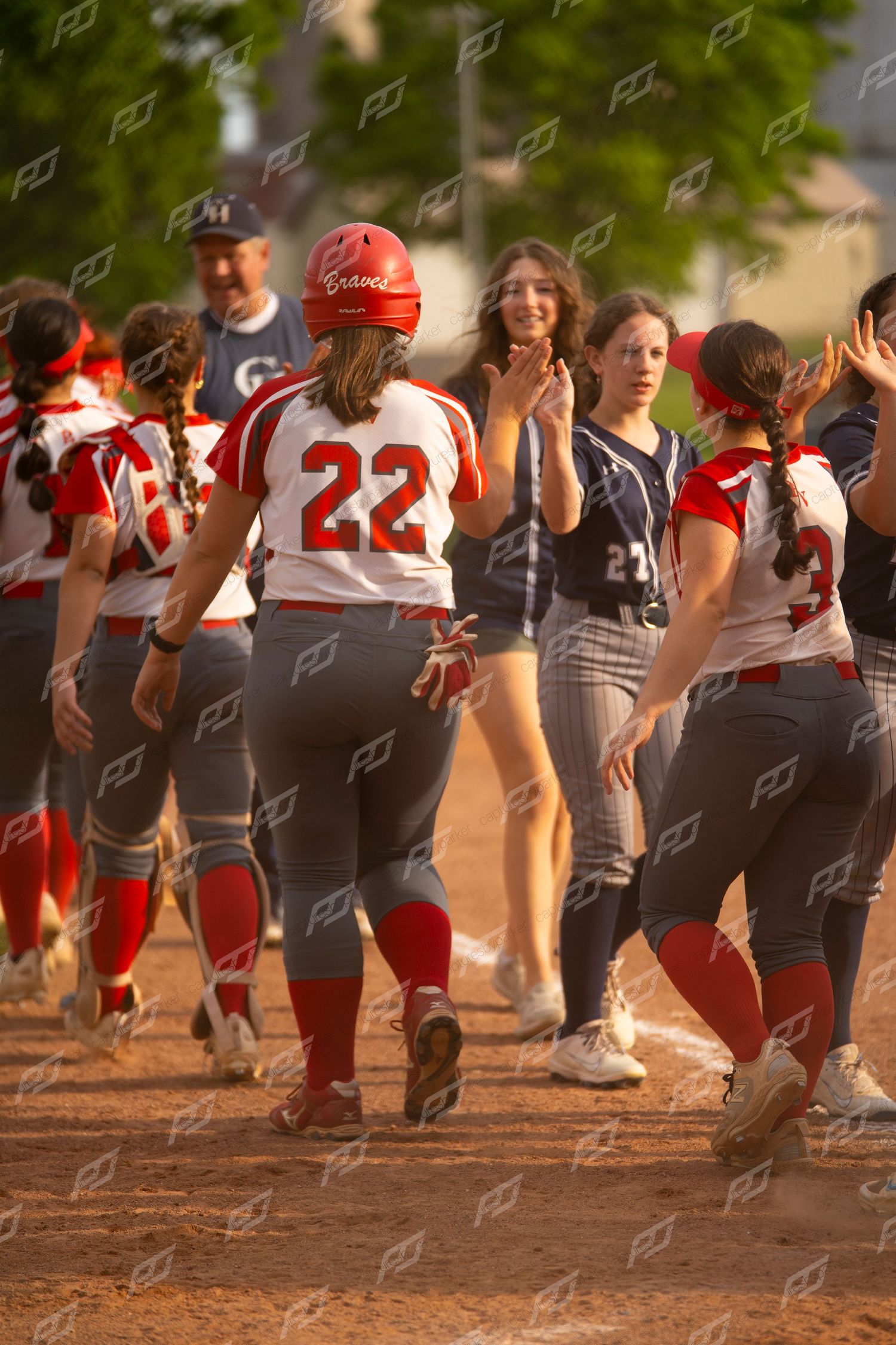 Softball players in red uniforms exchange high fives after scoring a run.