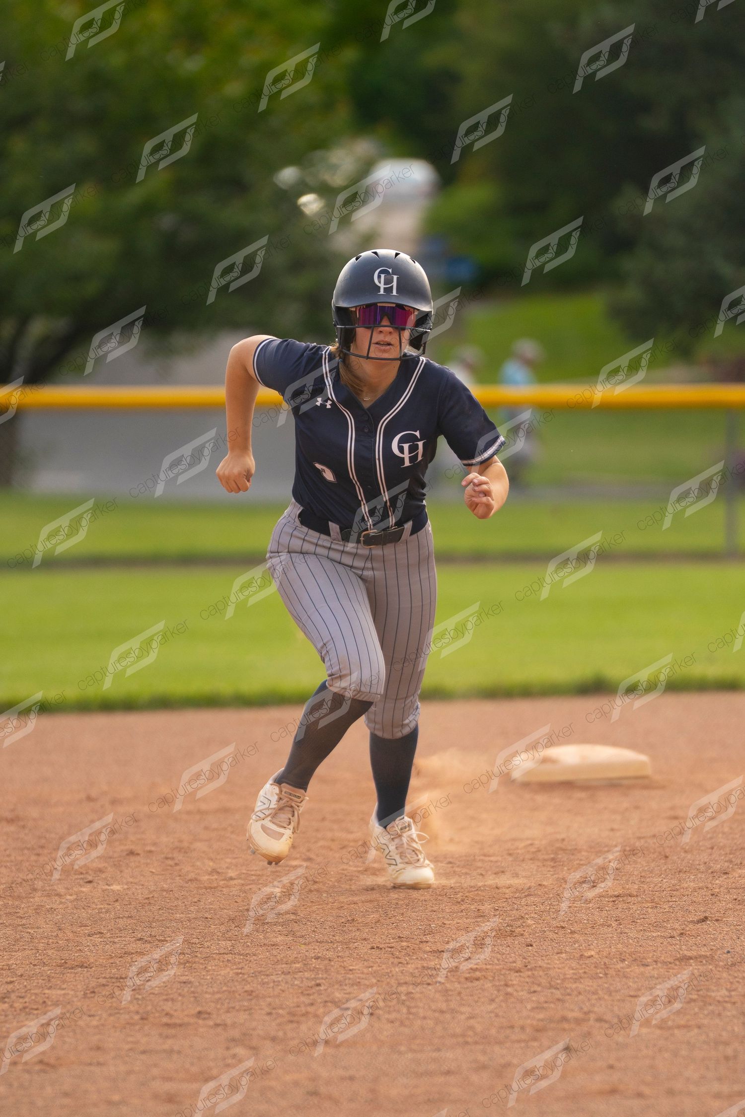 Female softball player in navy pinstripe uniform running bases during a game.