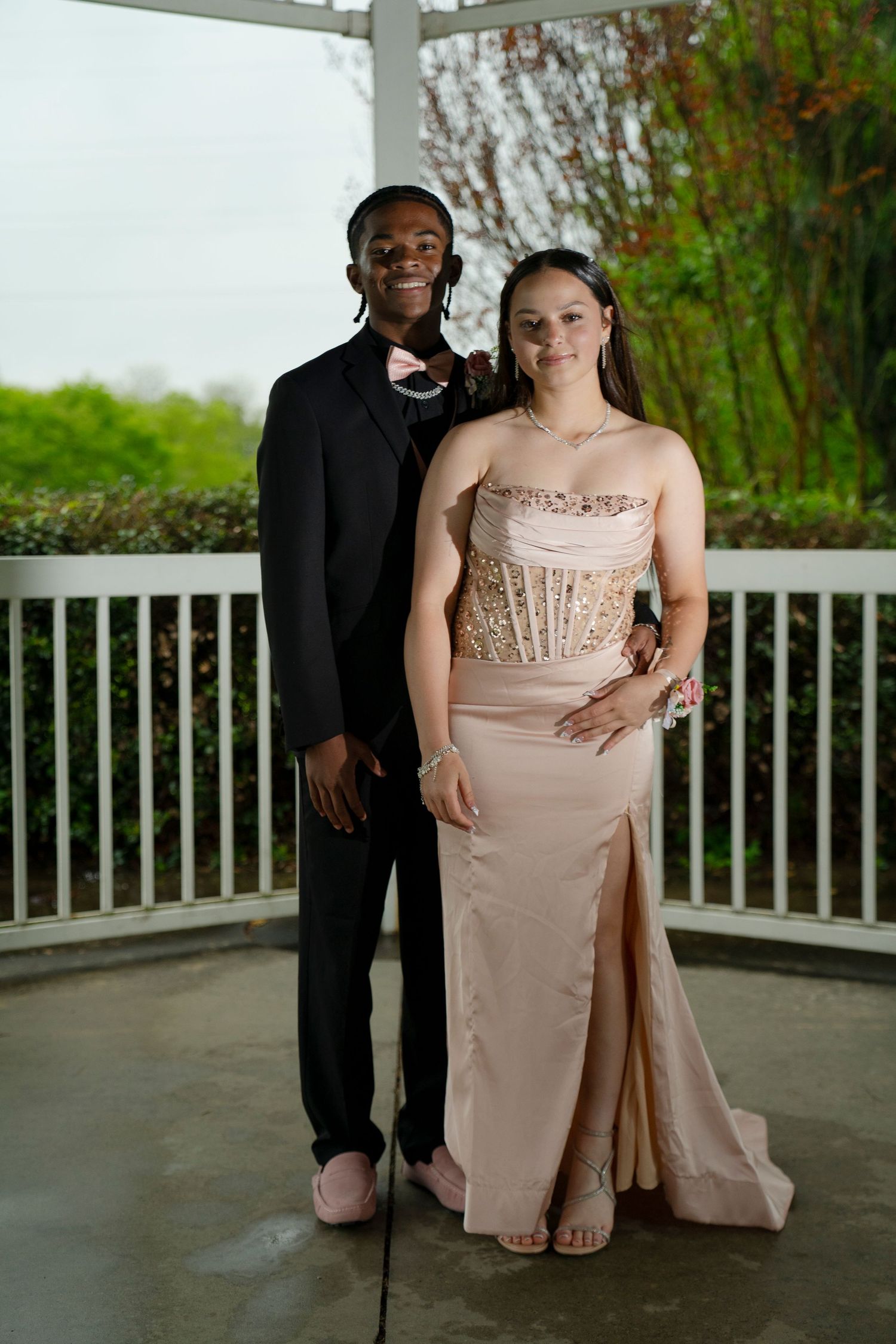 Prom couple poses together, young man in black tuxedo and woman in elegant champagne strapless gown.