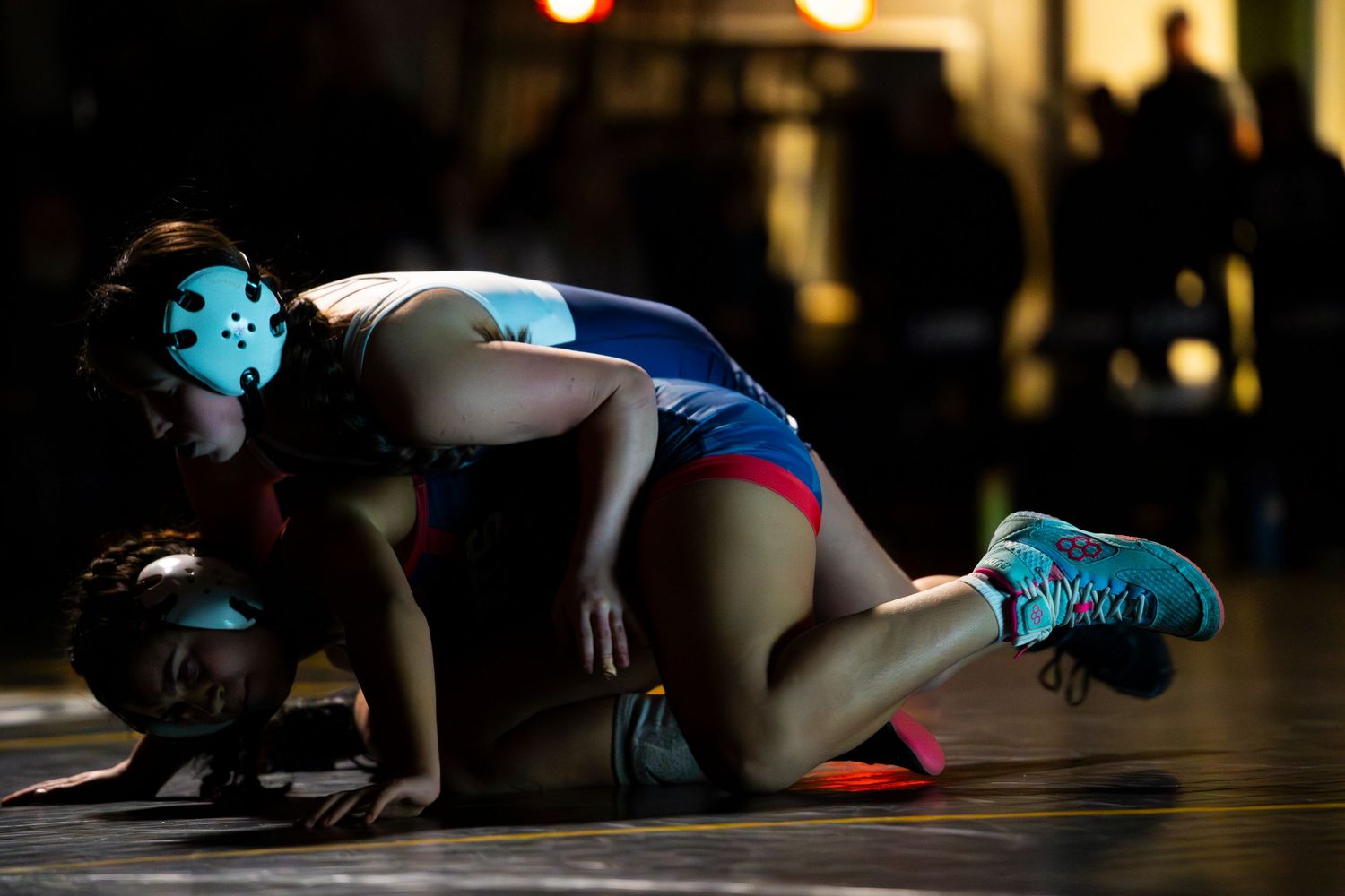 Female wrestler in blue singlet pins opponent on wrestling mat during competitive match.