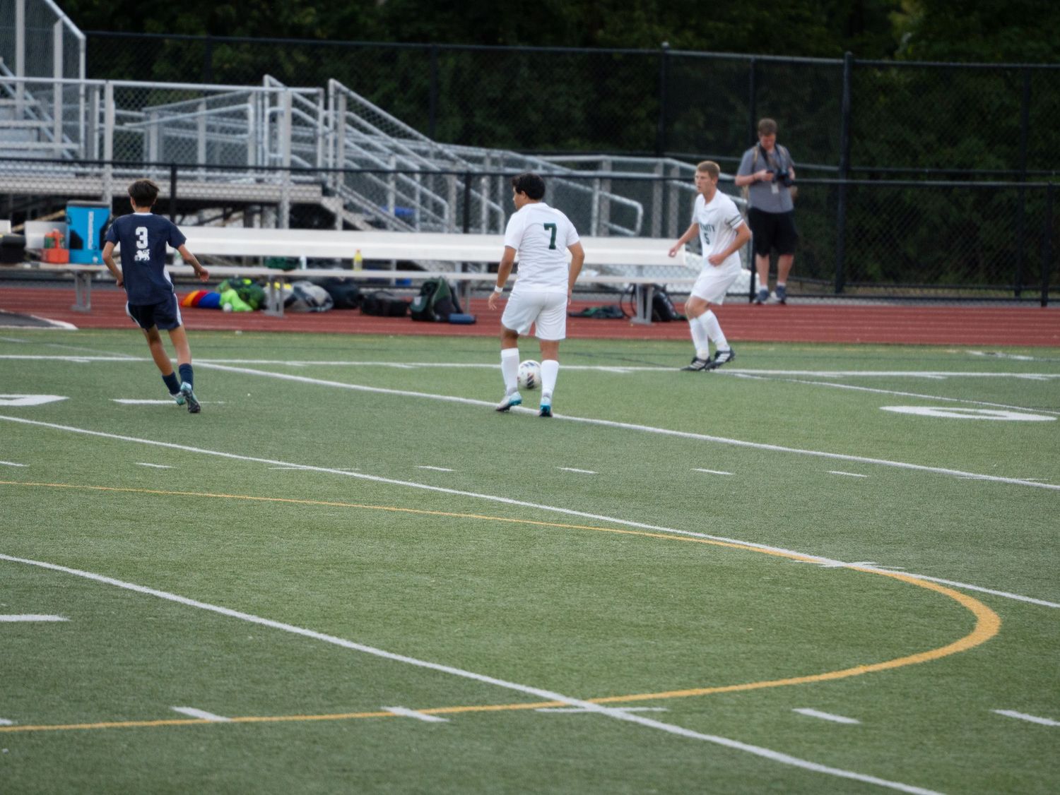 Two soccer players in navy and white uniforms compete for ball on green turf field.