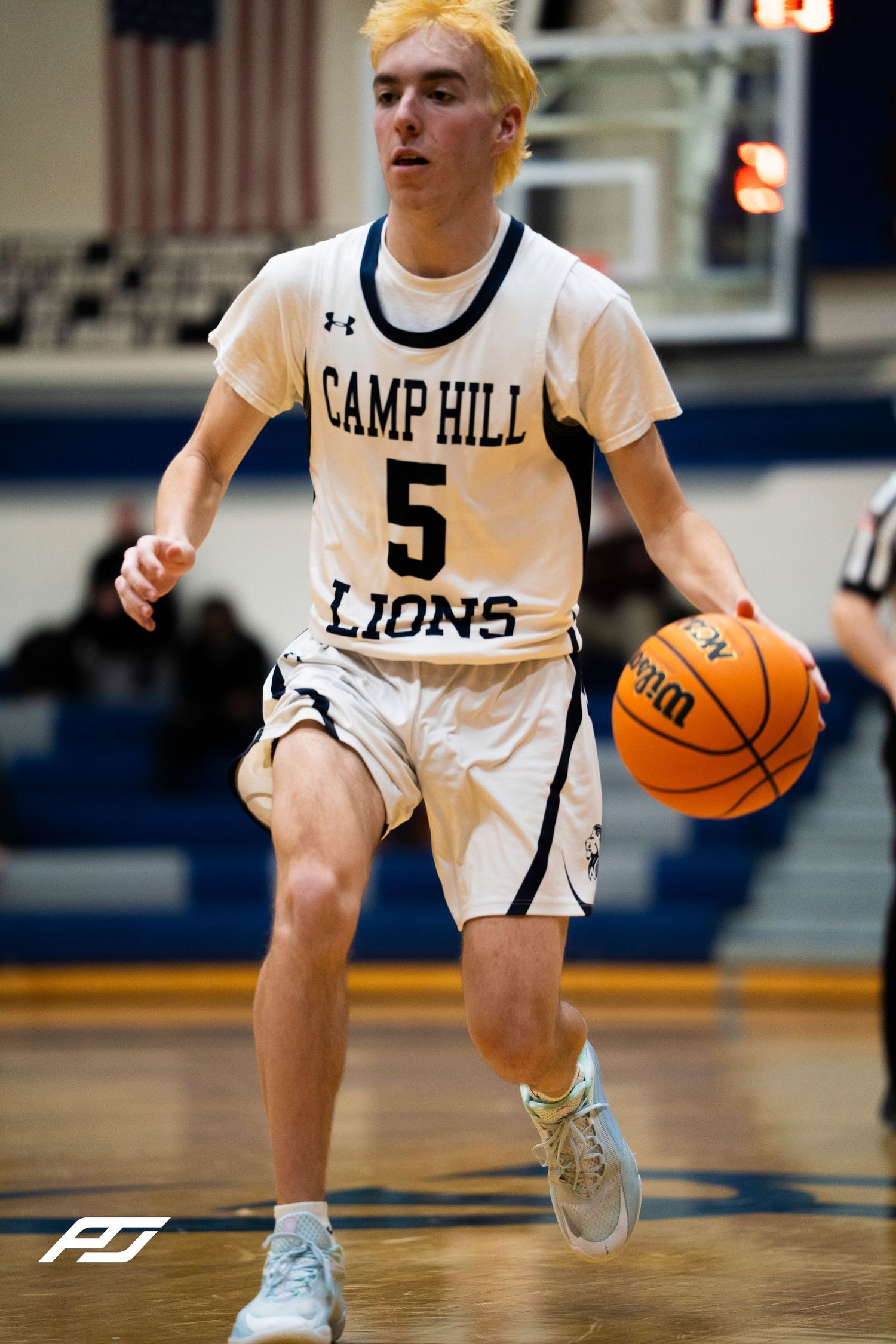 Camp Hill Lions #5 with blonde hair dribbles upcourt during a home basketball game.