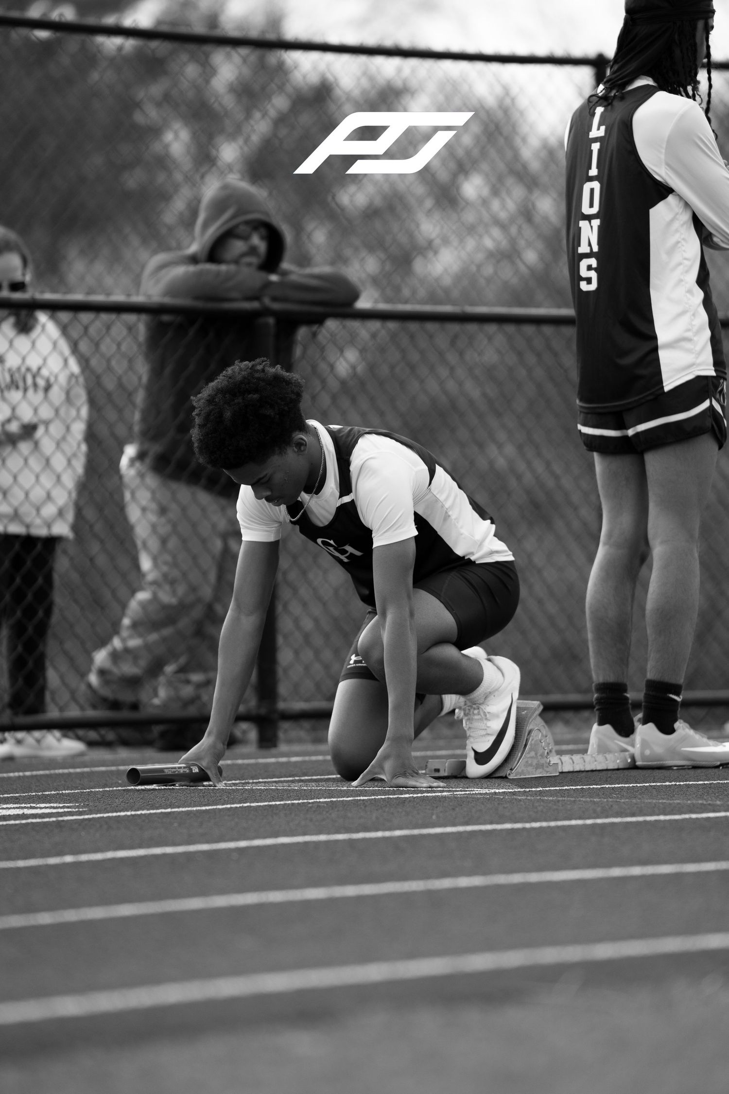Young track athlete sets up in starting position with baton on outdoor track lane.