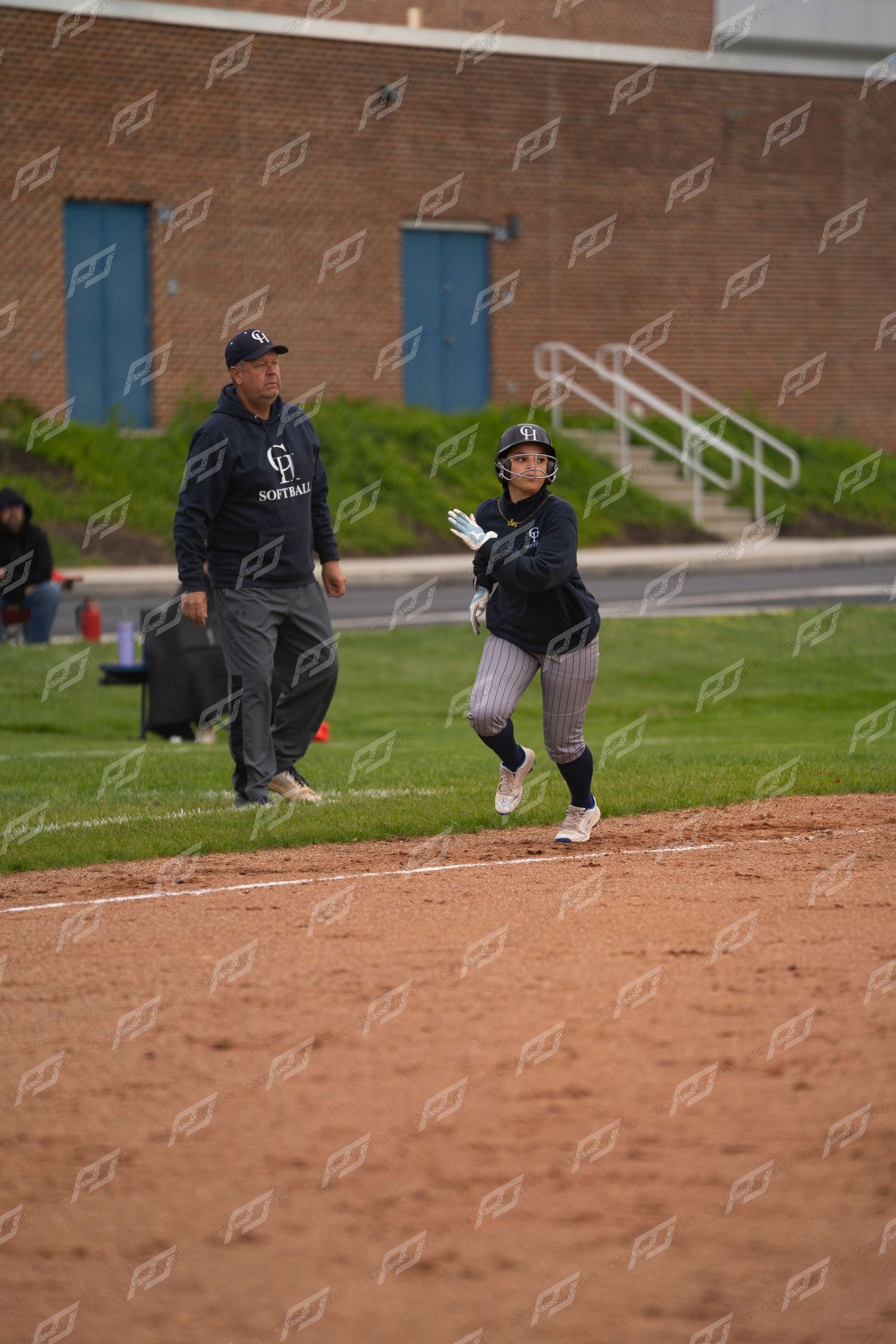 Softball player rounds third base with coach watching during a school game.