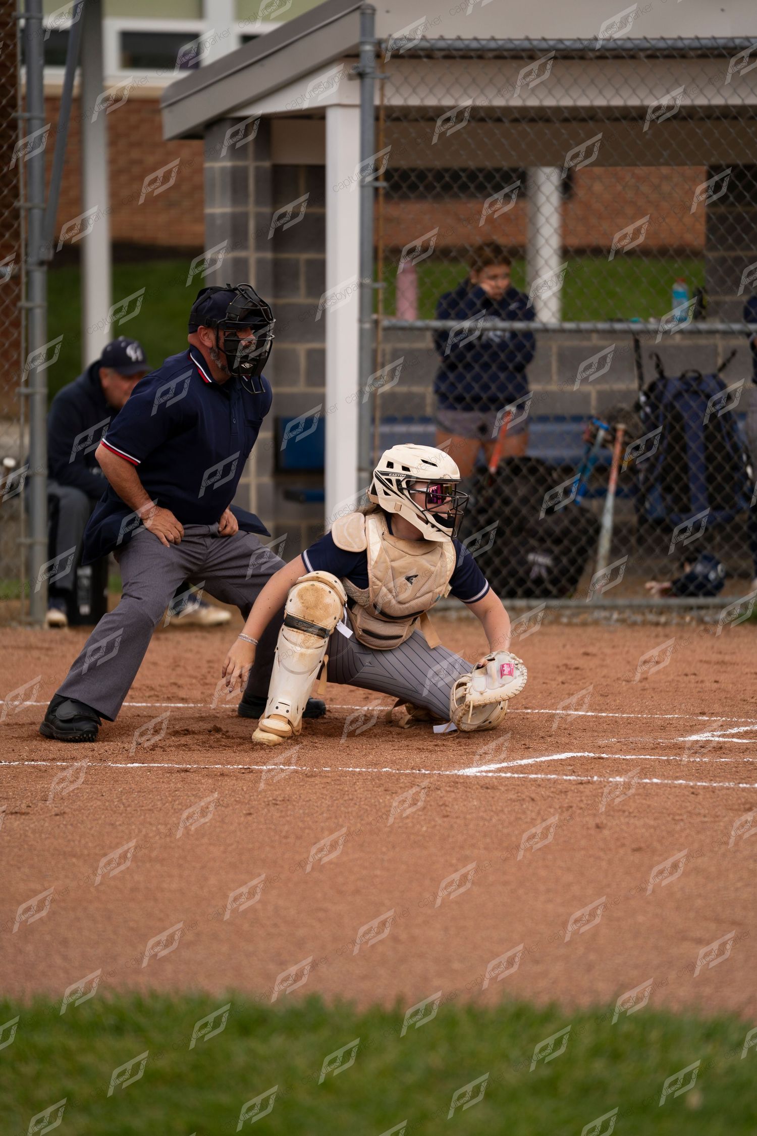 Female softball catcher in crouch position ready to receive a pitch with umpire behind her.