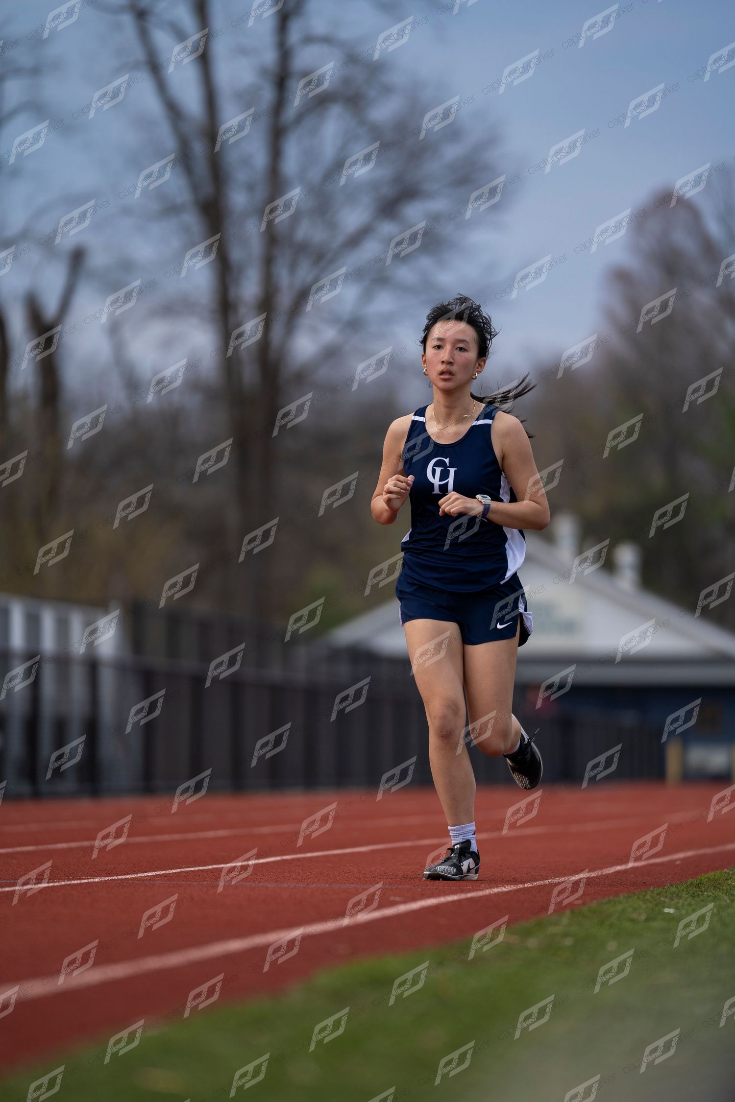 Female runner in navy CH uniform running solo on outdoor red track.