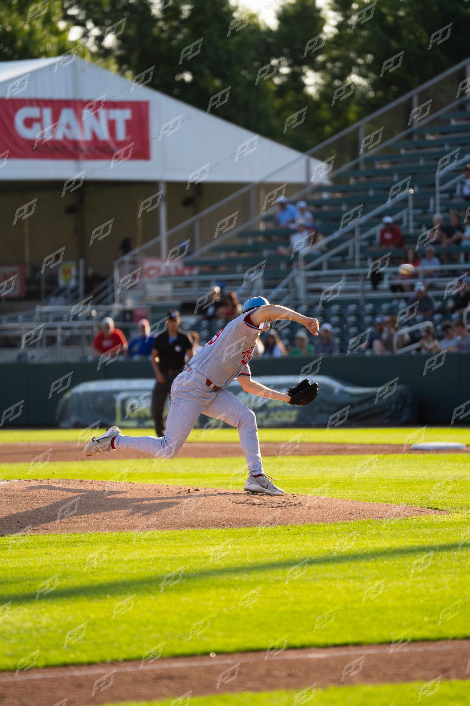 Baseball pitcher in white uniform delivering a pitch during an evening game with GIANT sign visible.