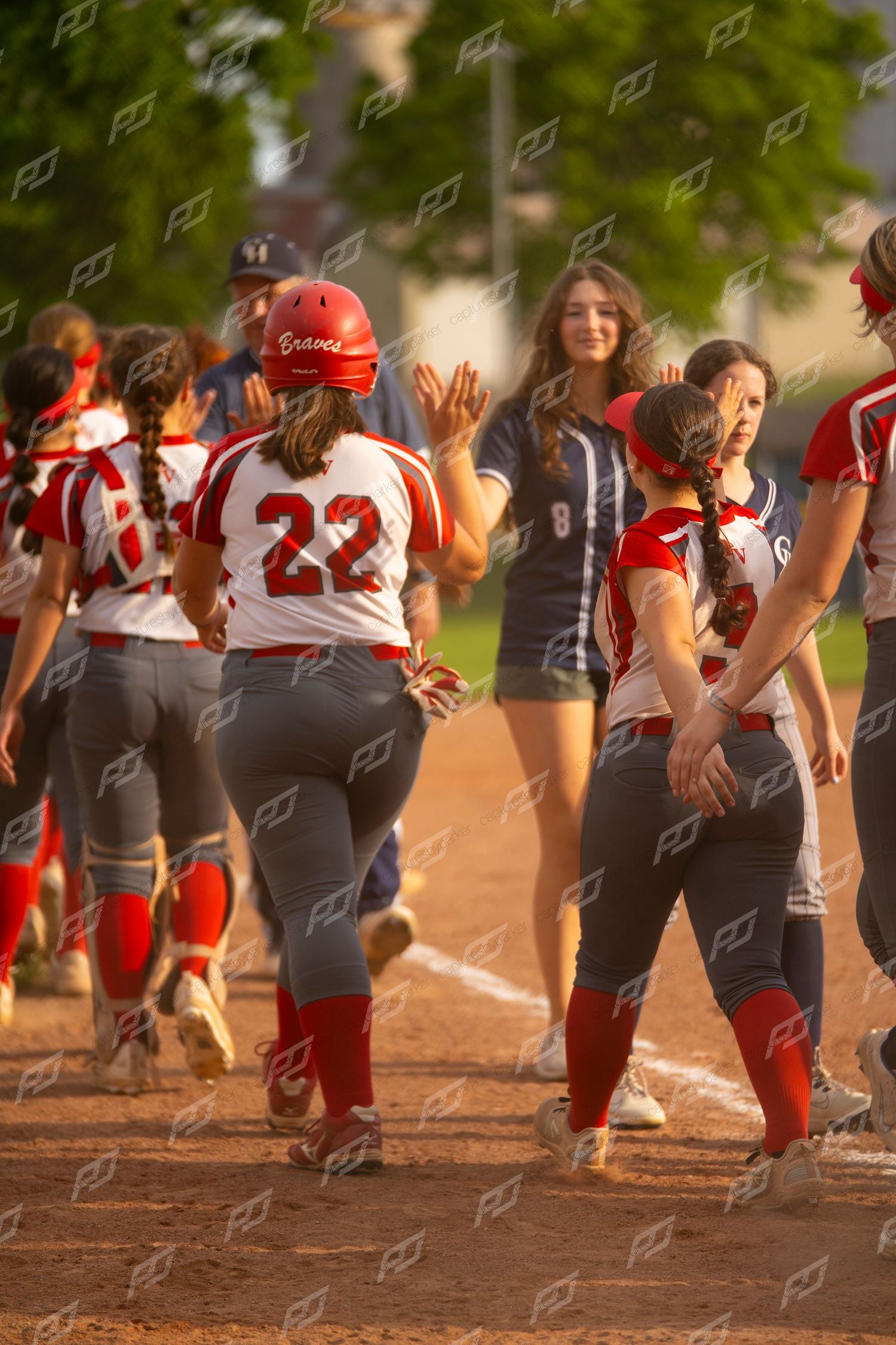 Female softball player number 22 in red uniform receives high fives from teammates.