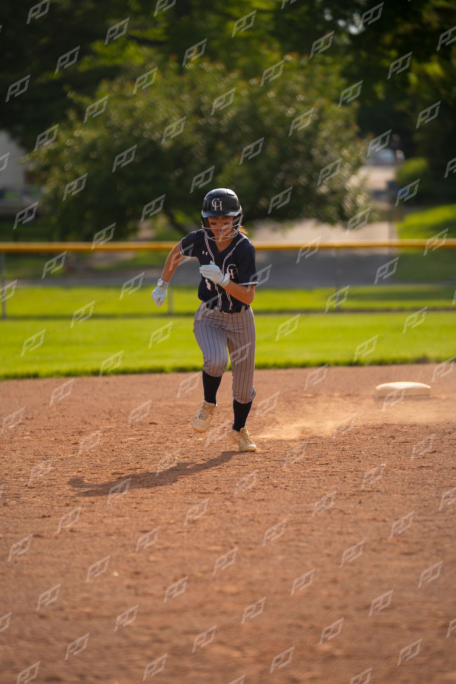 Female softball player running bases in navy pinstripe uniform kicking up dirt.