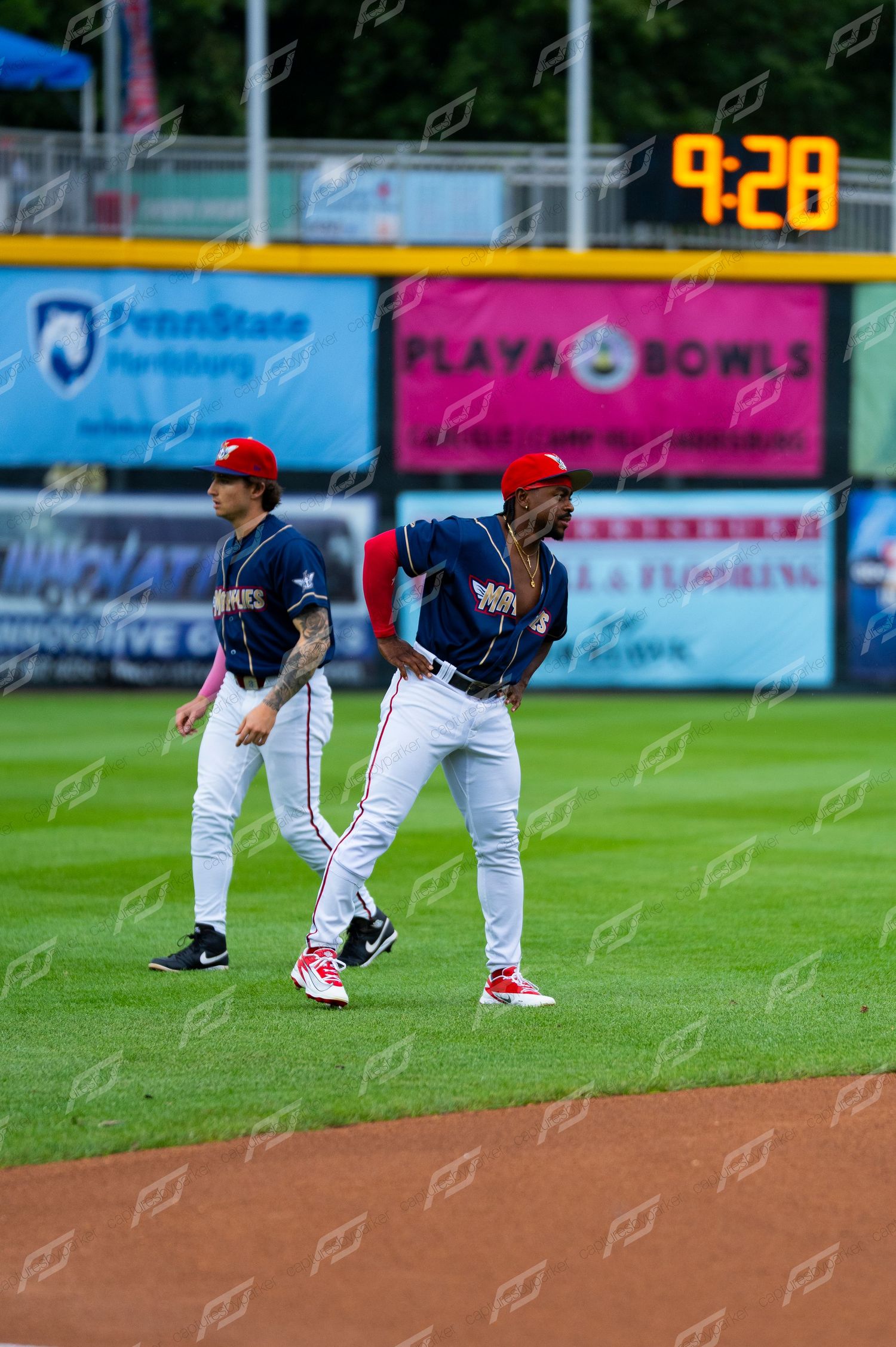 Two minor league baseball players in navy uniforms walk across the outfield during warmups.