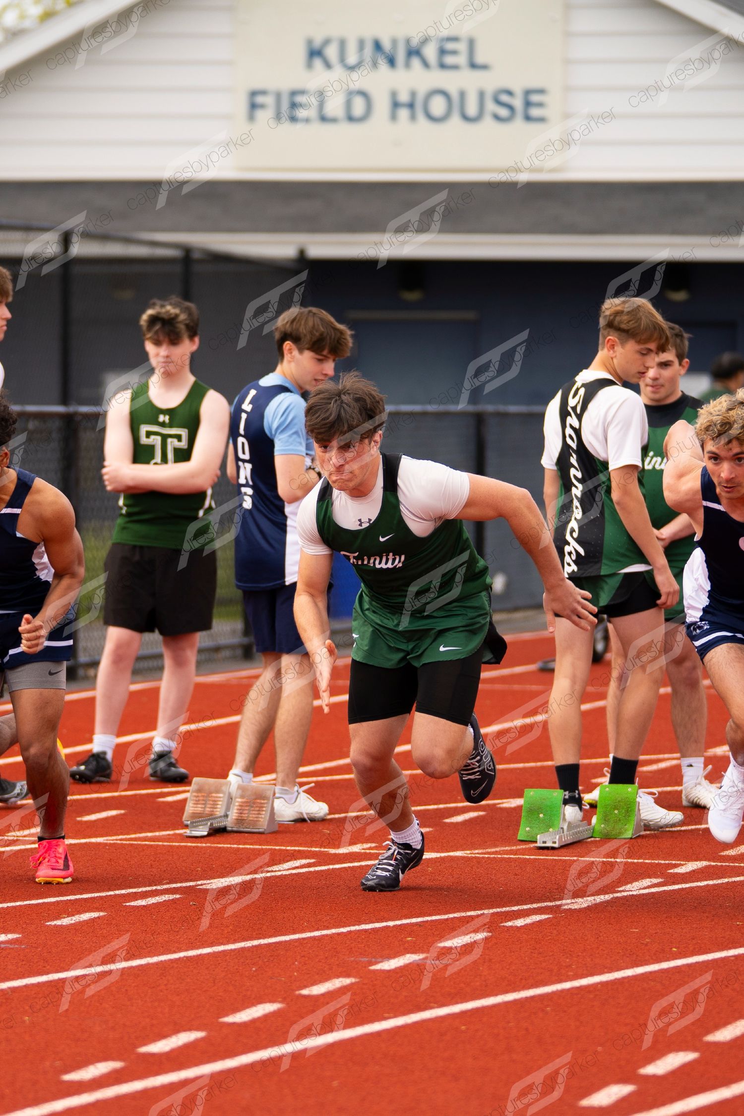 Male sprinter in green Shamrocks jersey bursts from starting blocks at Kunkel Field House track meet.