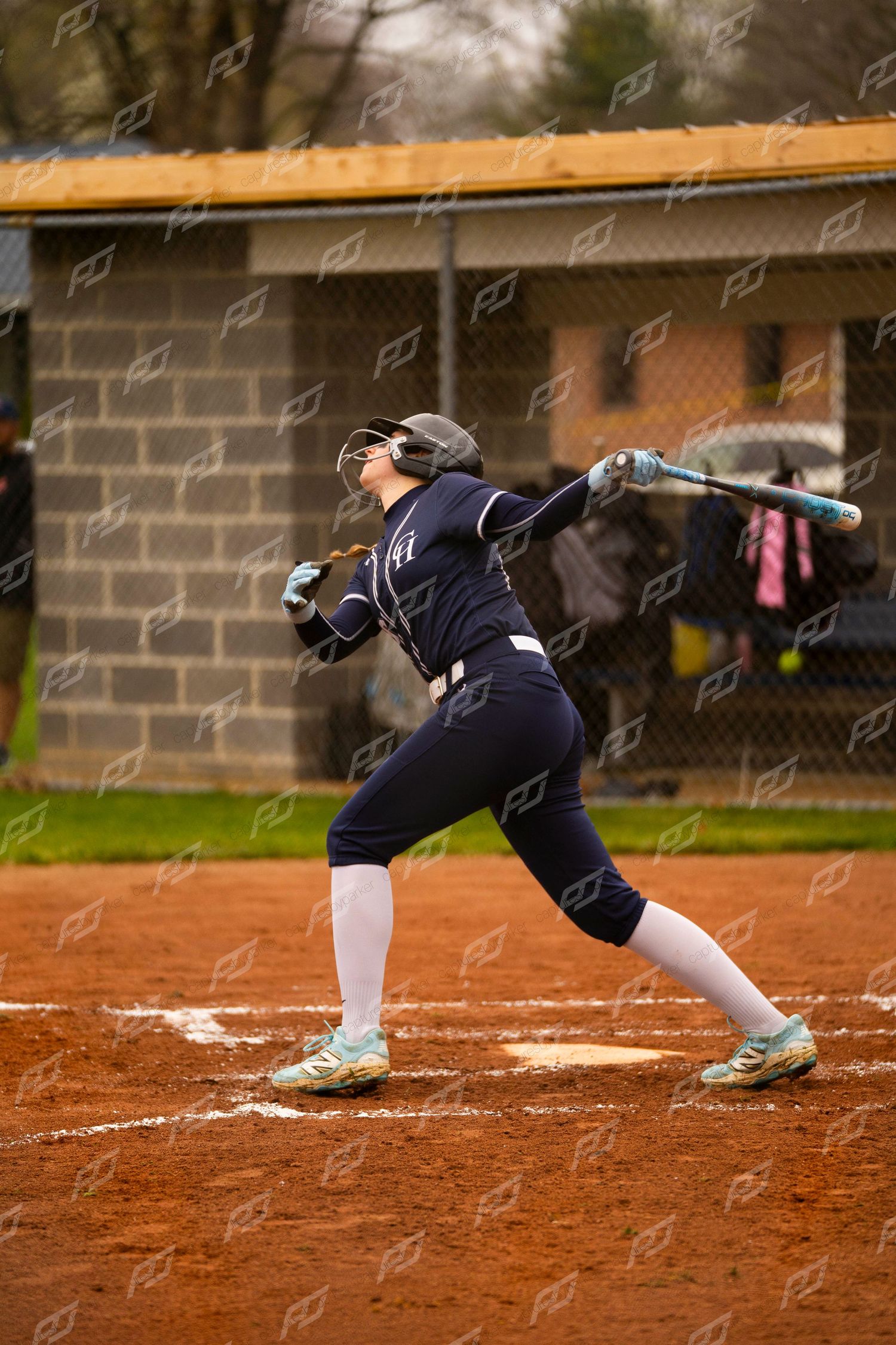 Softball player in navy uniform follows through on a swing with a blue bat during a game.