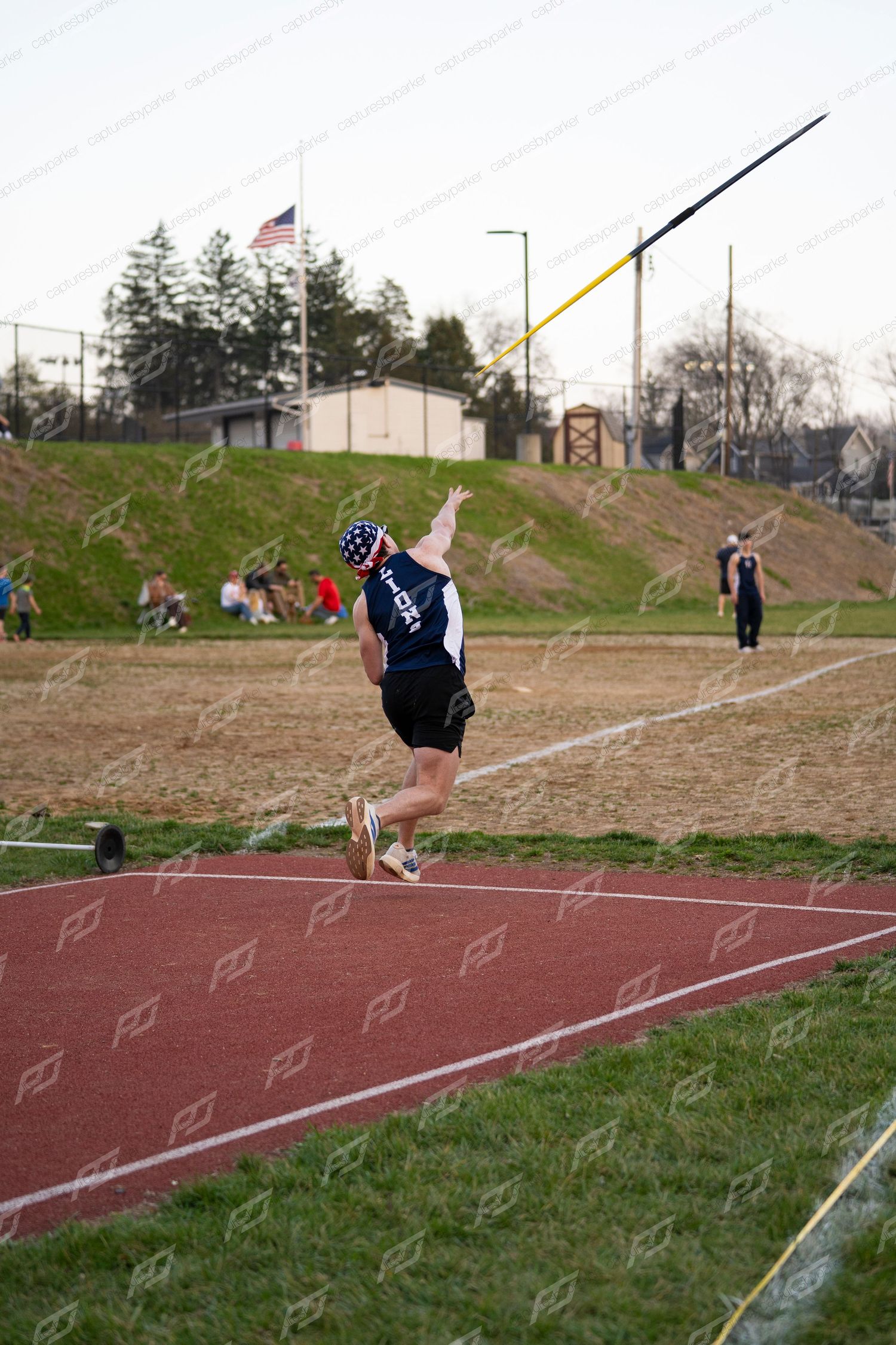 Track athlete follows through on javelin throw during outdoor high school track and field meet.