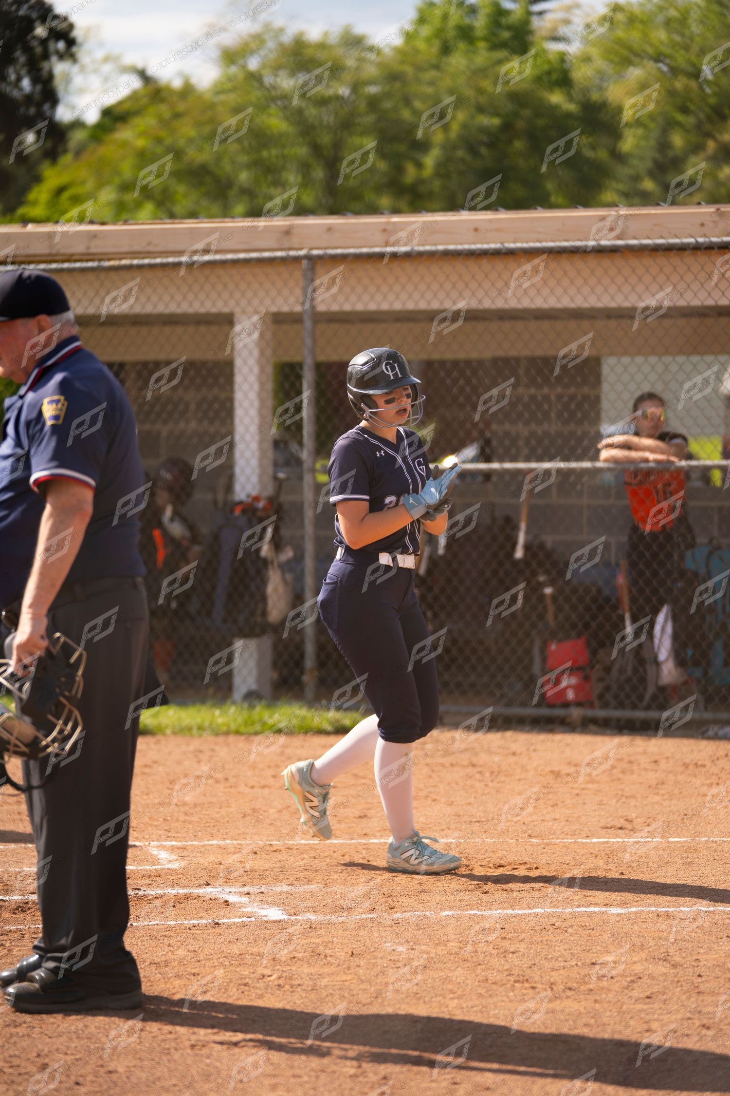 Smiling softball player in navy uniform crosses home plate as an umpire watches nearby.