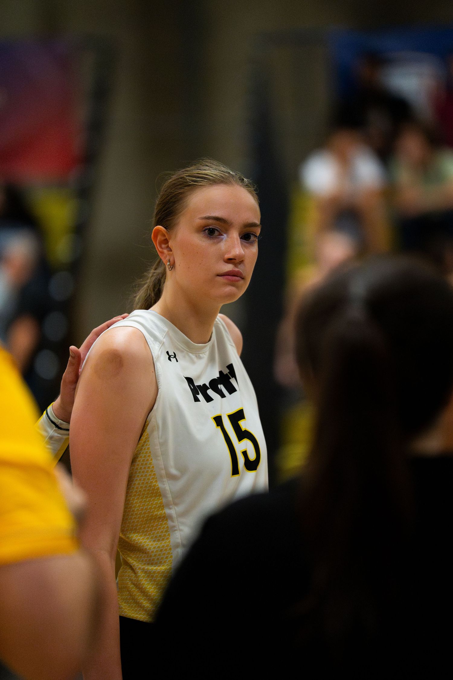Female volleyball player wearing number 15 jersey stands focused during a competitive indoor volleyball match.