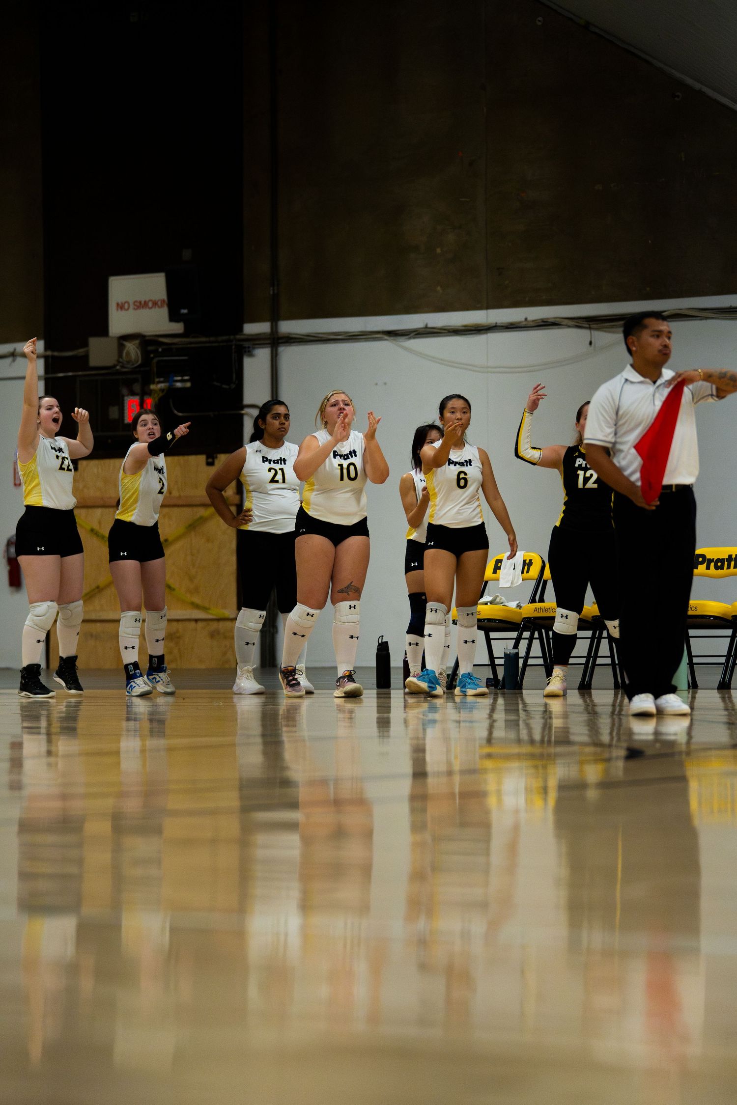 Volleyball team celebrating on the sideline in black and white uniforms with coach raising hand.