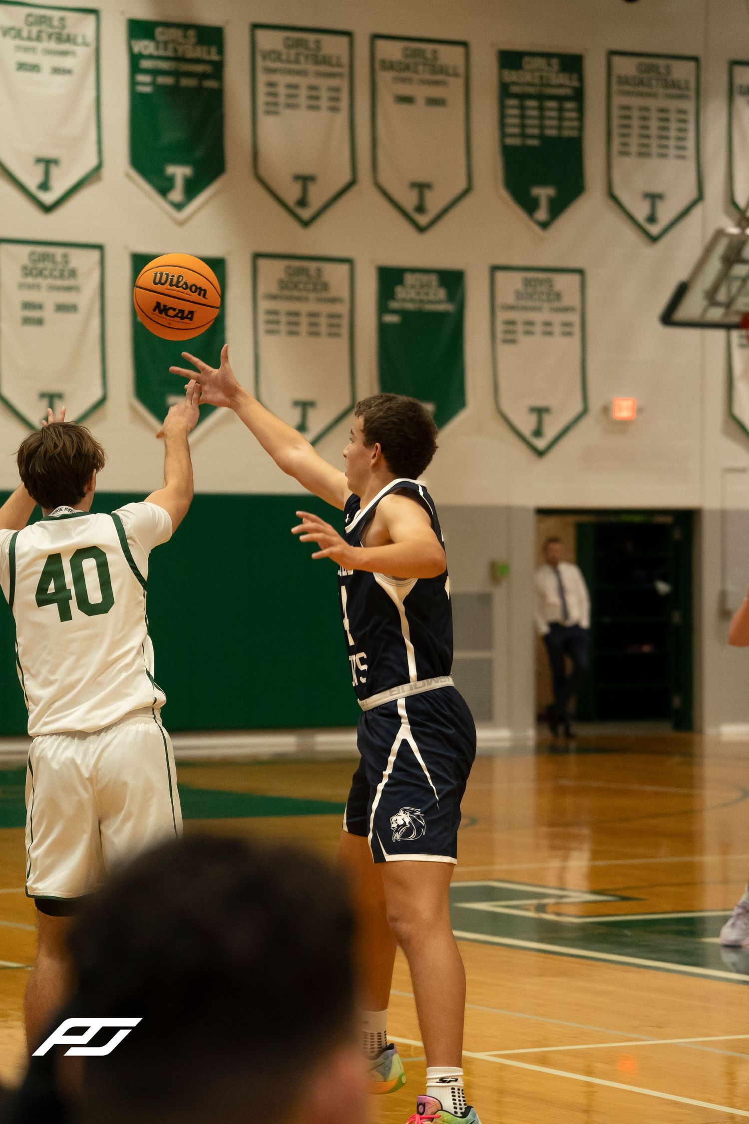 Basketball player in navy uniform attempts a jump shot over defender wearing number 40 green jersey.