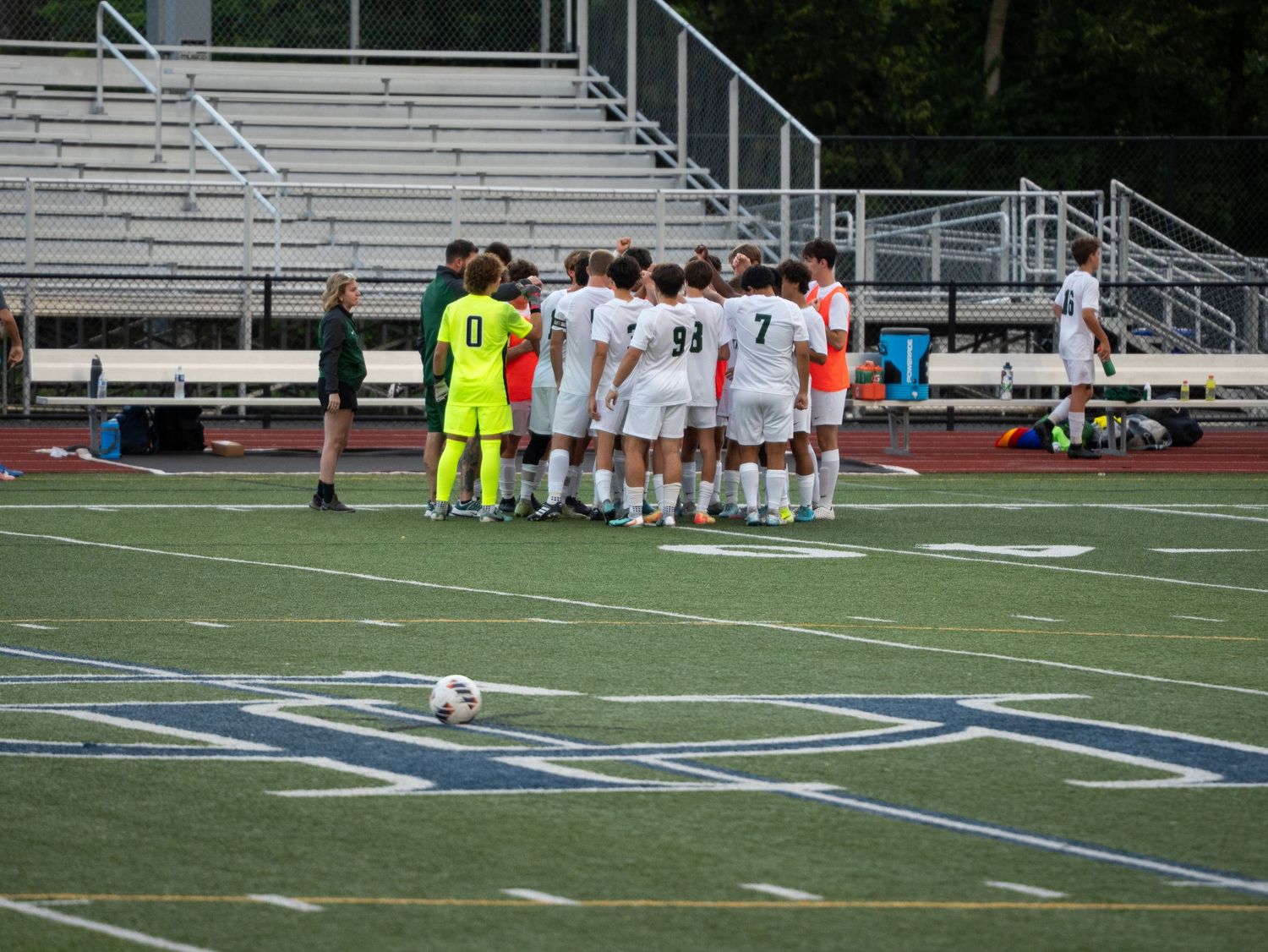 Trinity soccer team huddles together on blue turf field before game with goalkeeper in yellow.