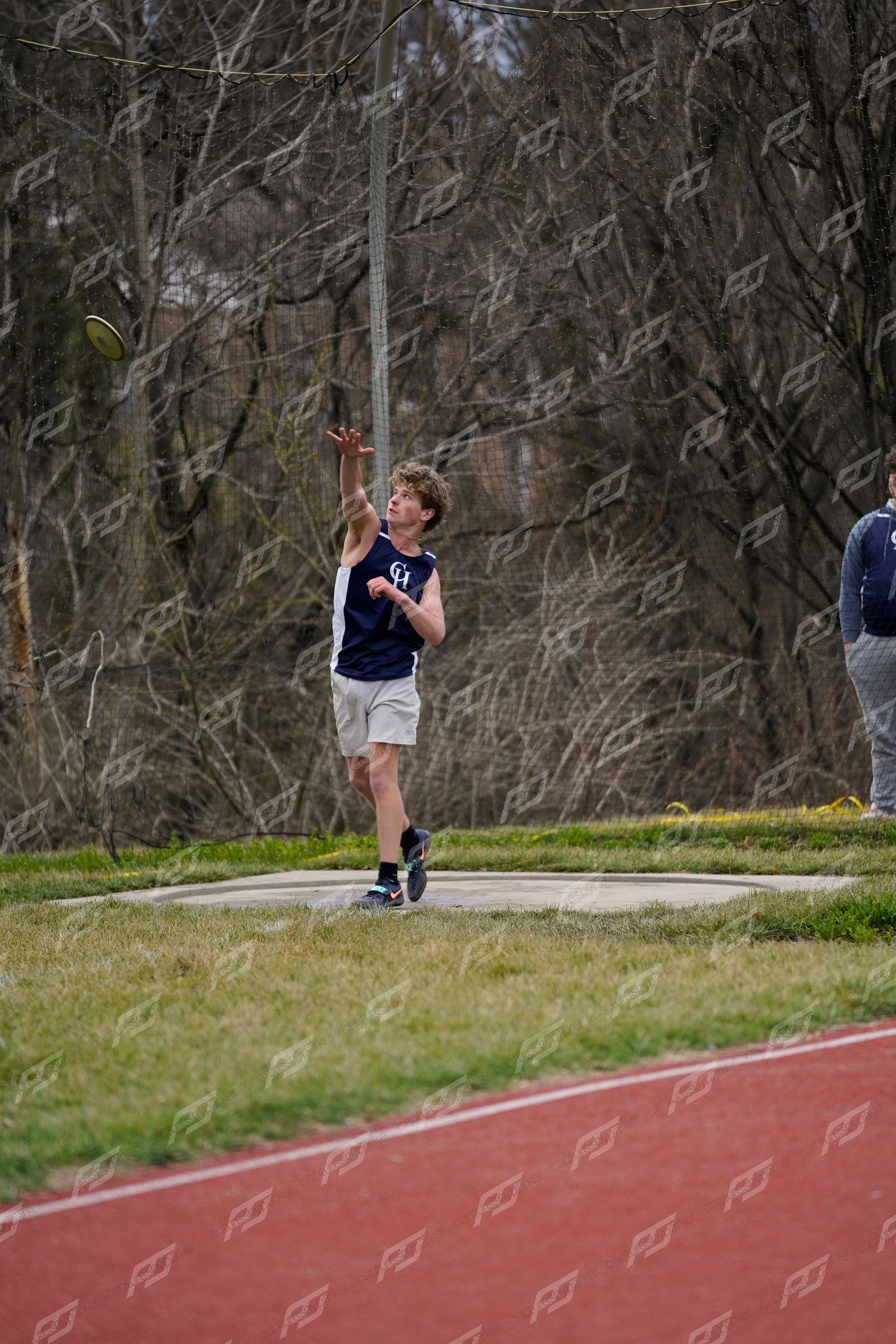 Male athlete releasing a discus throw during an outdoor high school track and field meet.