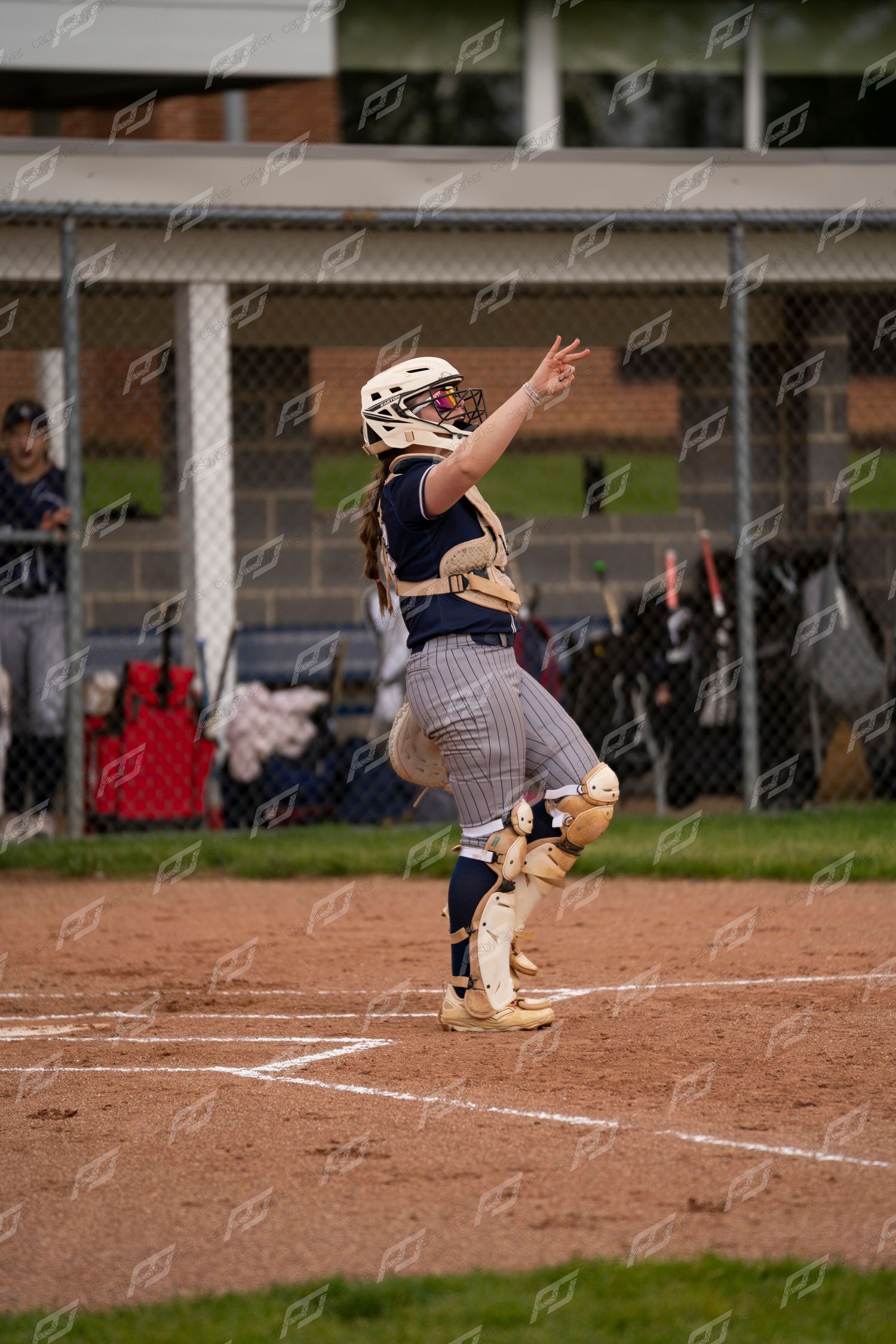 Female softball catcher in full gear leaping to catch a ball during a game.